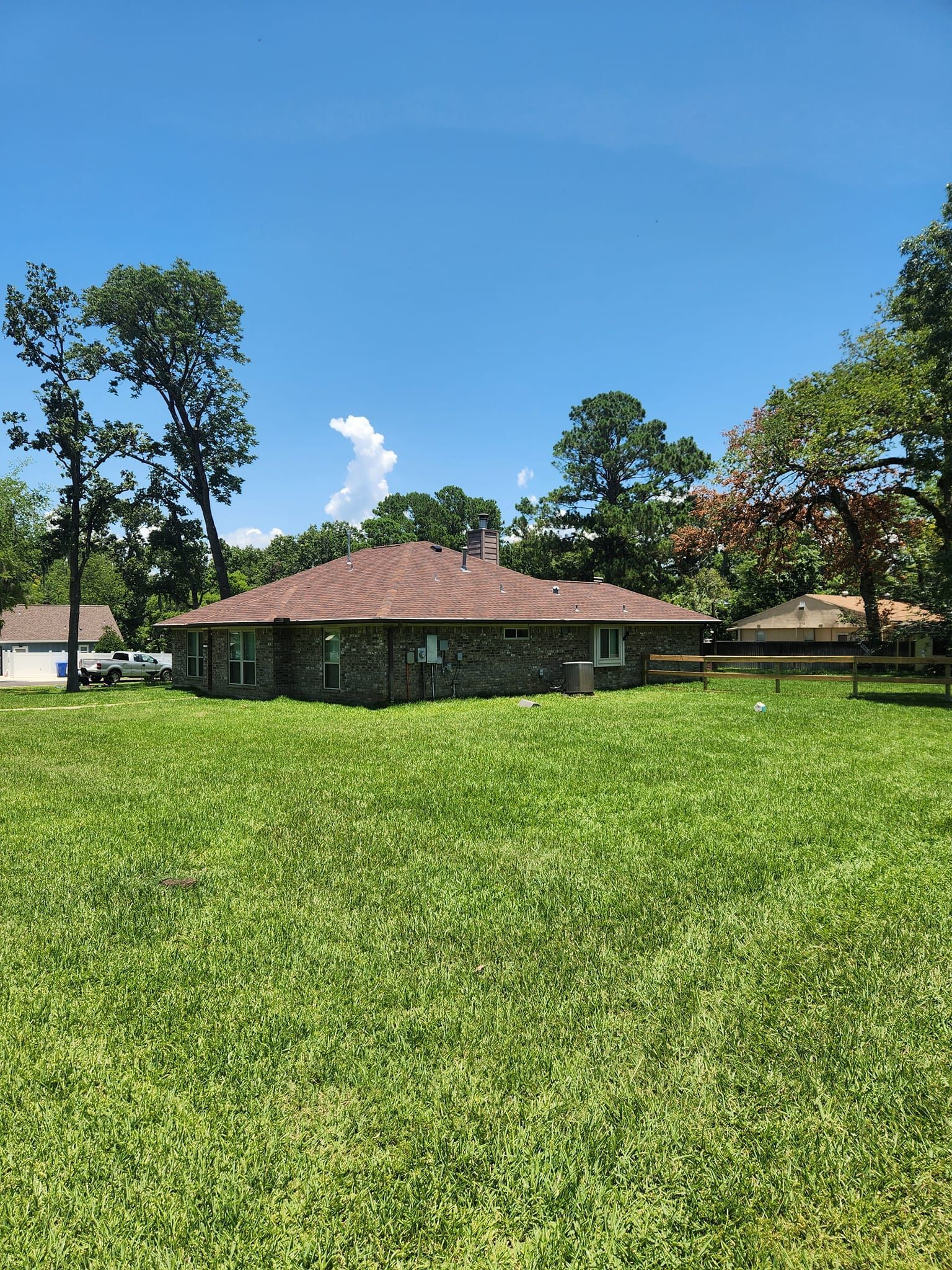 Single-story house with a red roof in a sunny grassy field under a clear blue sky.