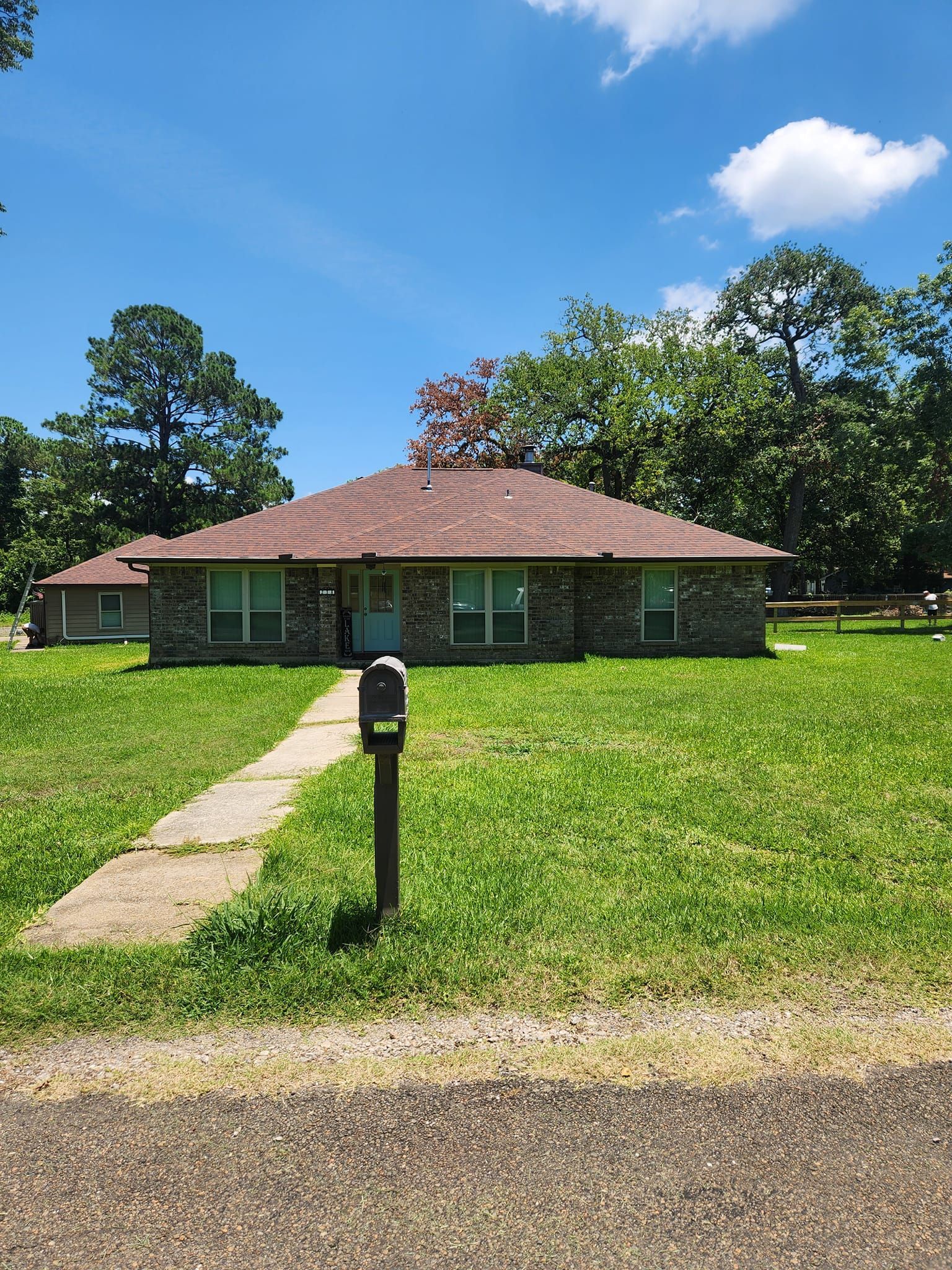 Single-story stone house with a red roof, mailbox, and front lawn under a blue sky