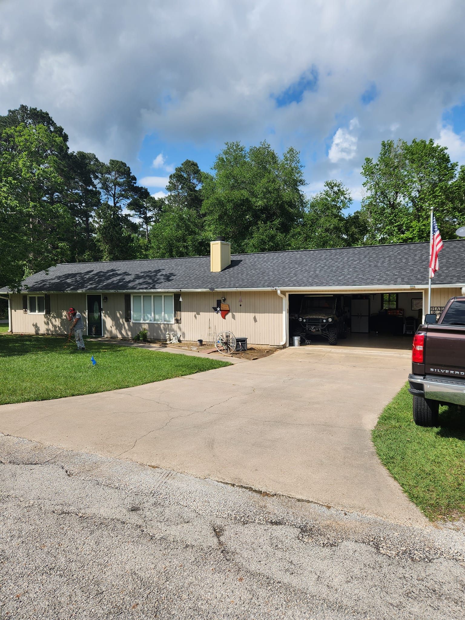 Single-story house with a gravel driveway, open garage, and American flag under a partly cloudy sky