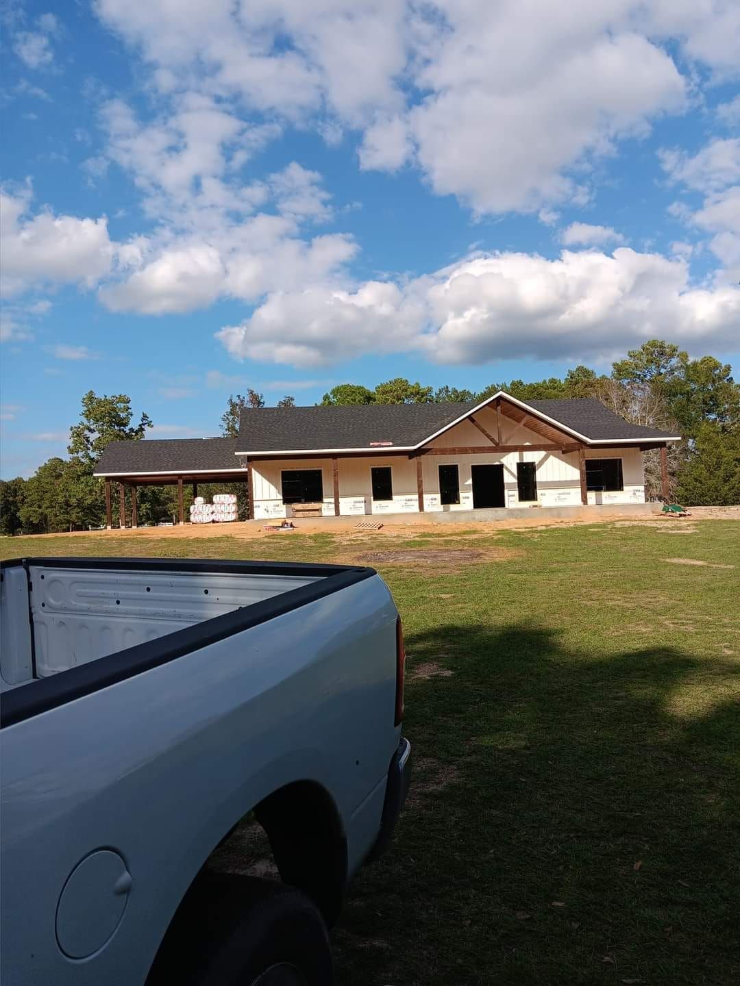 White pickup truck in foreground with a single-story house and cloudy blue sky in the background