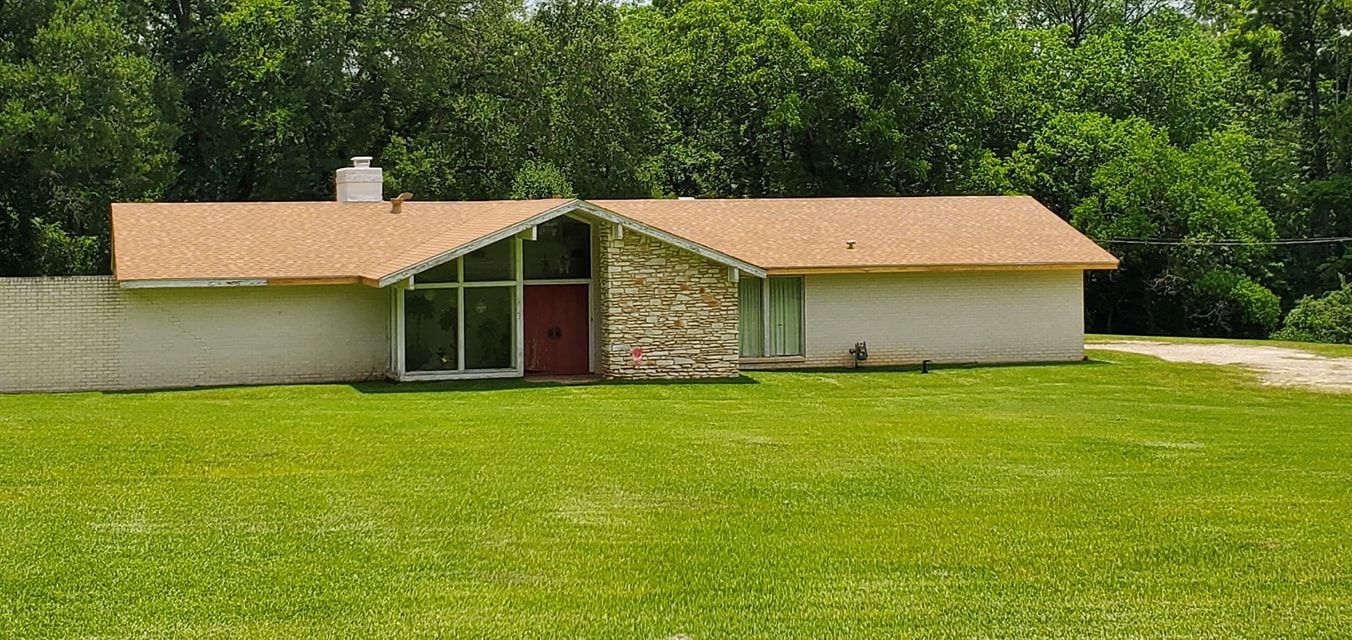 Small beige house with a red door, tan roof, and stone center on a grassy lawn