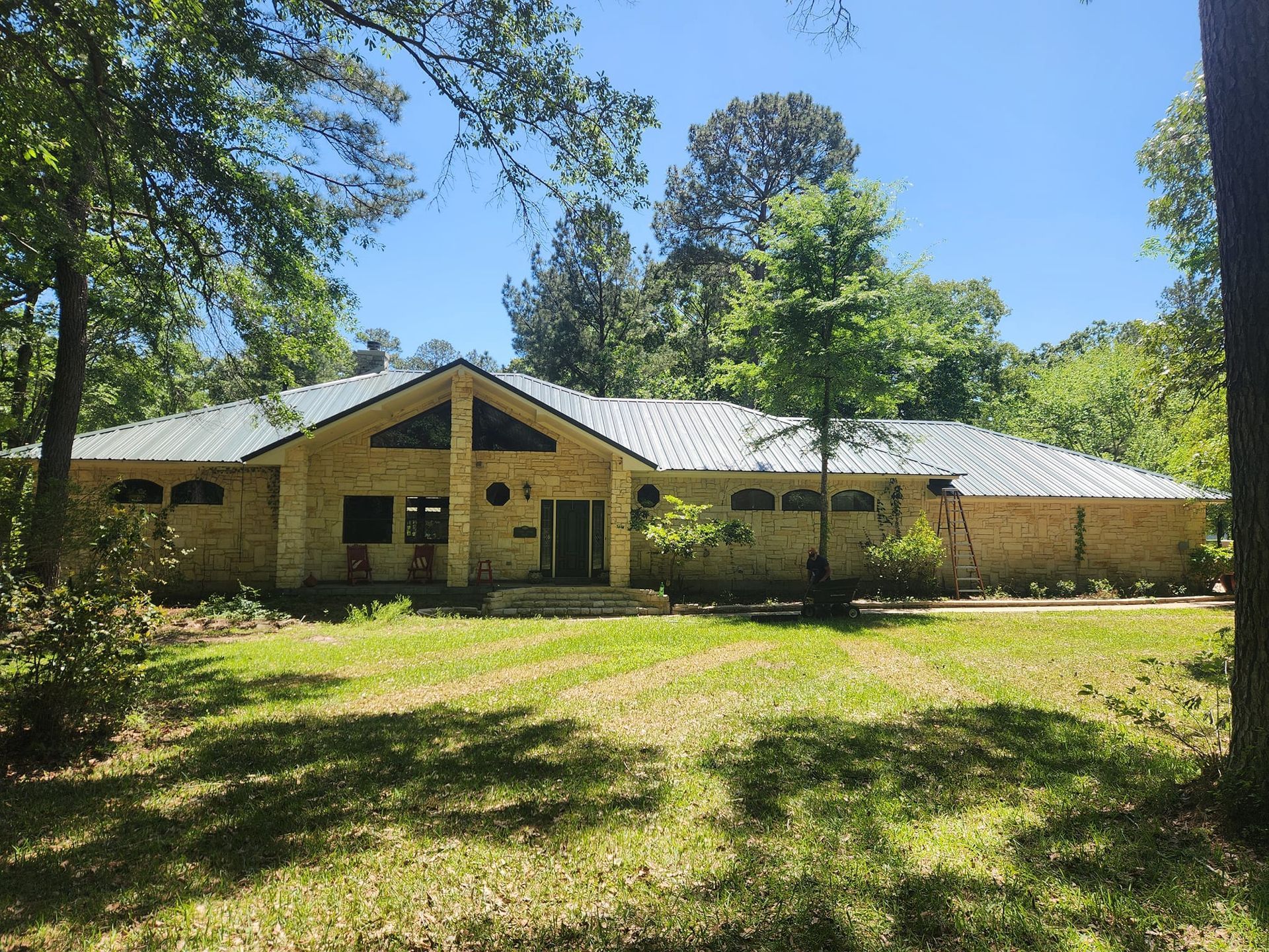Single-story beige building with a triangular entry, surrounded by trees and sunlit grass