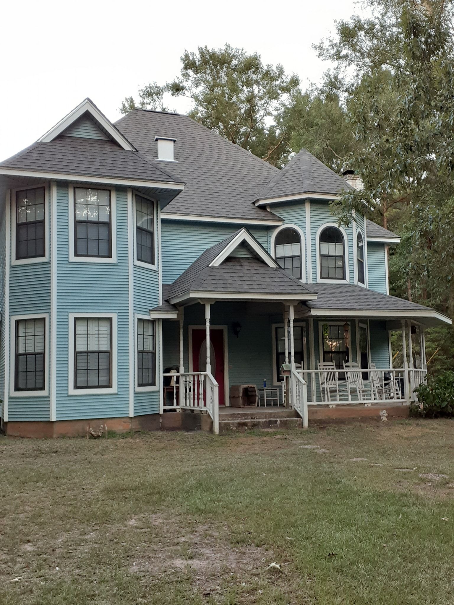 Blue Victorian-style house with a covered porch and dormer windows, set in a grassy yard.