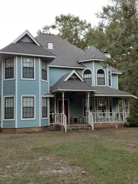 Two-story light blue house with white trim and a covered front porch in a grassy yard