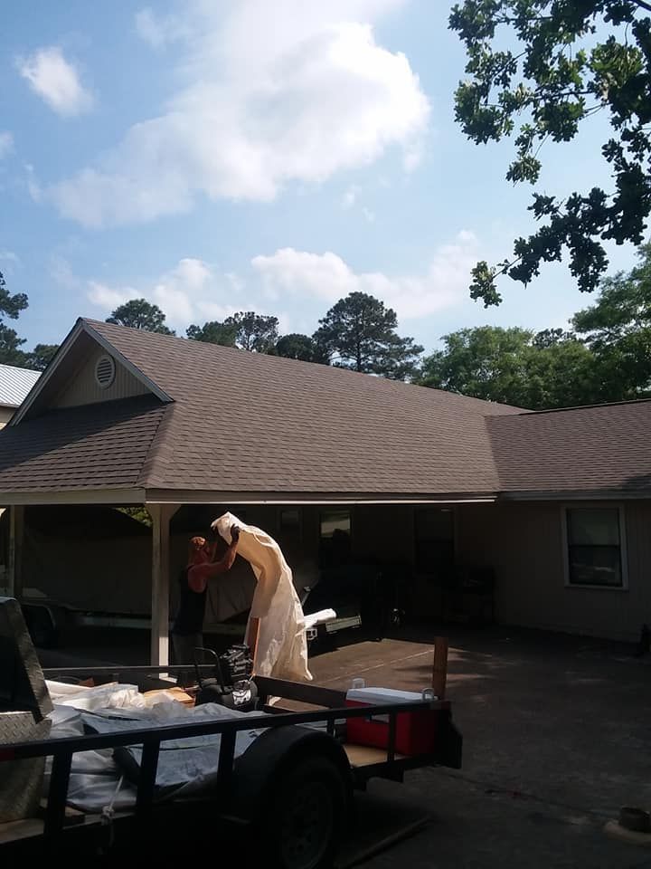Person loading items into a trailer in a driveway beside a suburban house under a partly cloudy sky