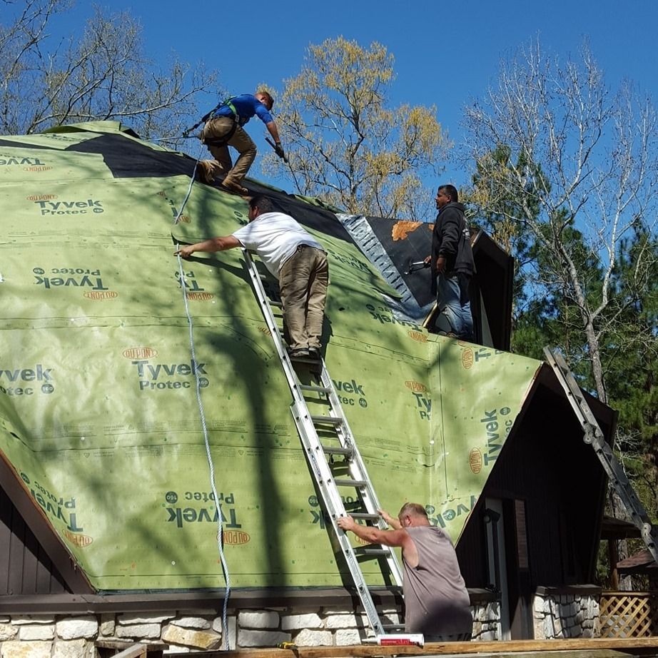 Workers on a roof installing green roofing felt beside a ladder and cabin structure