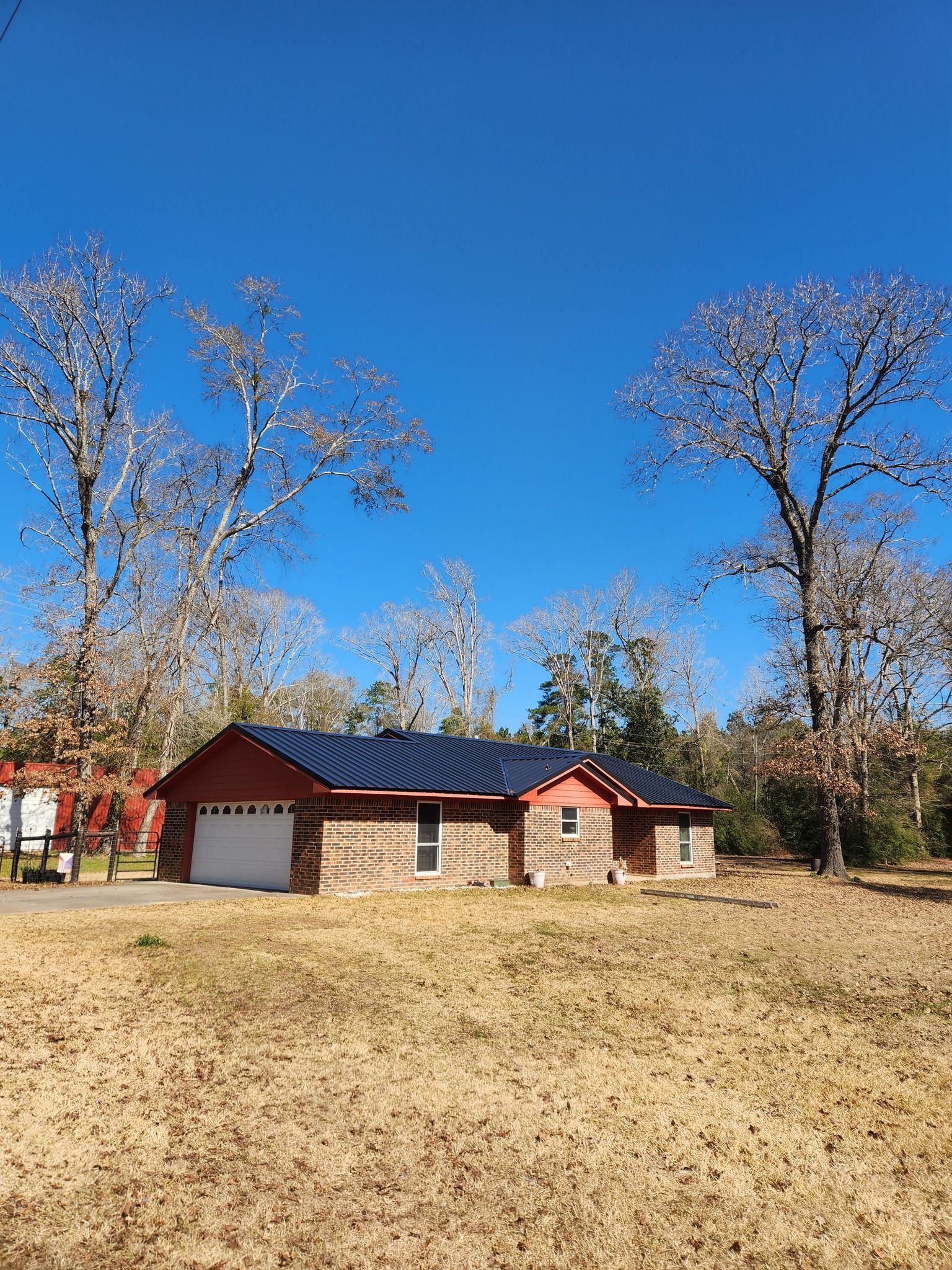 Red brick house with a red roof on a dry grassy lot under a clear blue sky