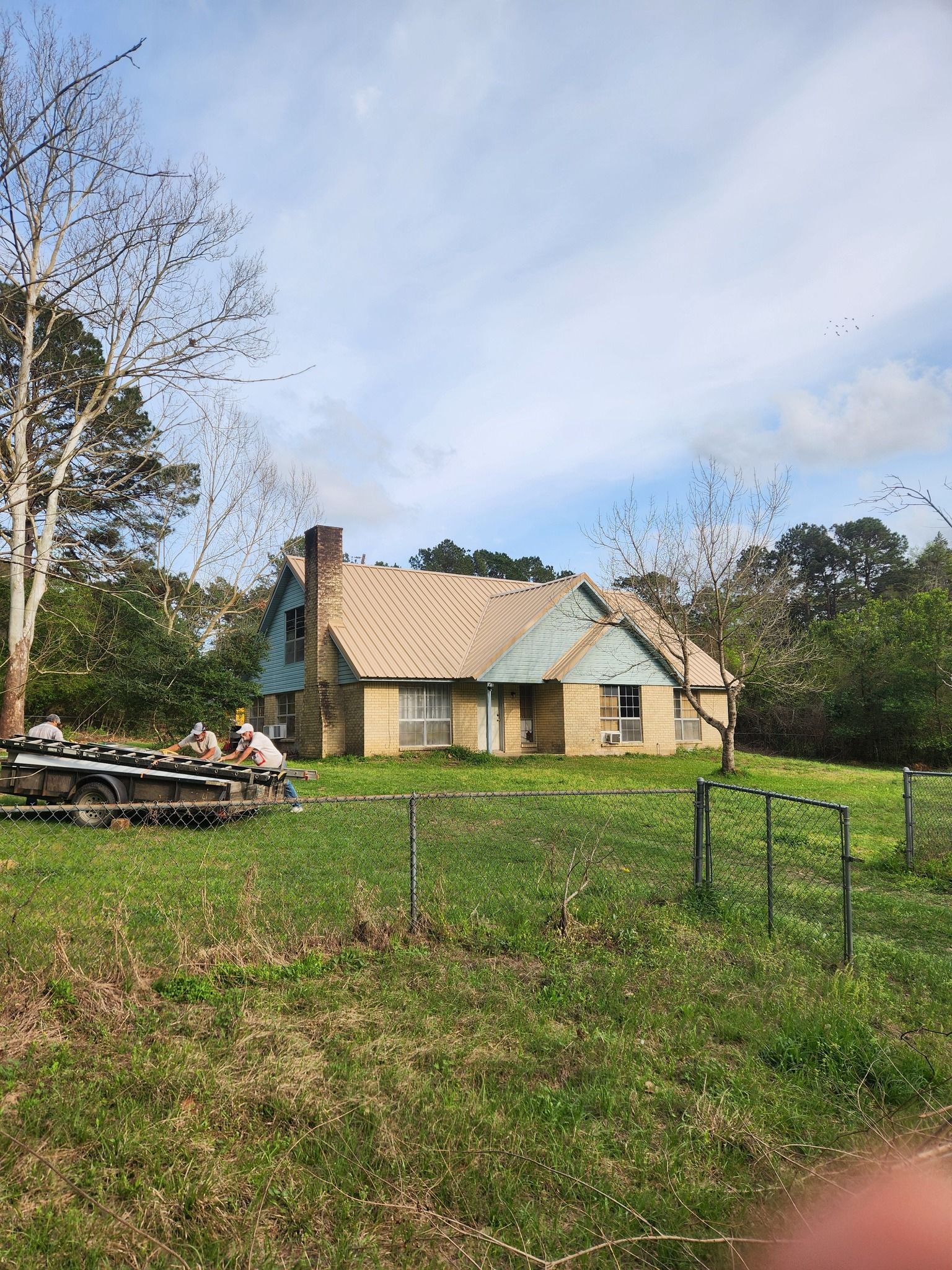 Small rustic cottage with a tan roof in a grassy field under a partly cloudy sky.