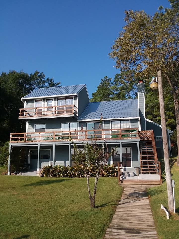 Two-story blue house with a porch, stairs, and a grassy front lawn under a clear sky