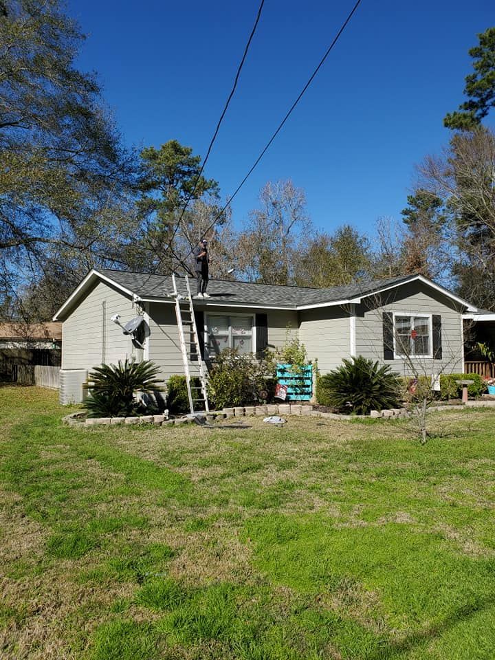 Small gray house with a ladder on the front, green lawn, and trees under a blue sky.