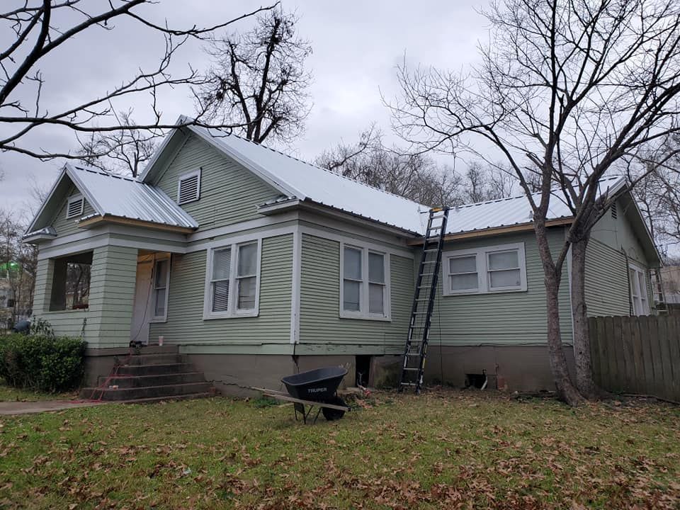 Small green house with a snow-dusted roof and leafless trees in a yard