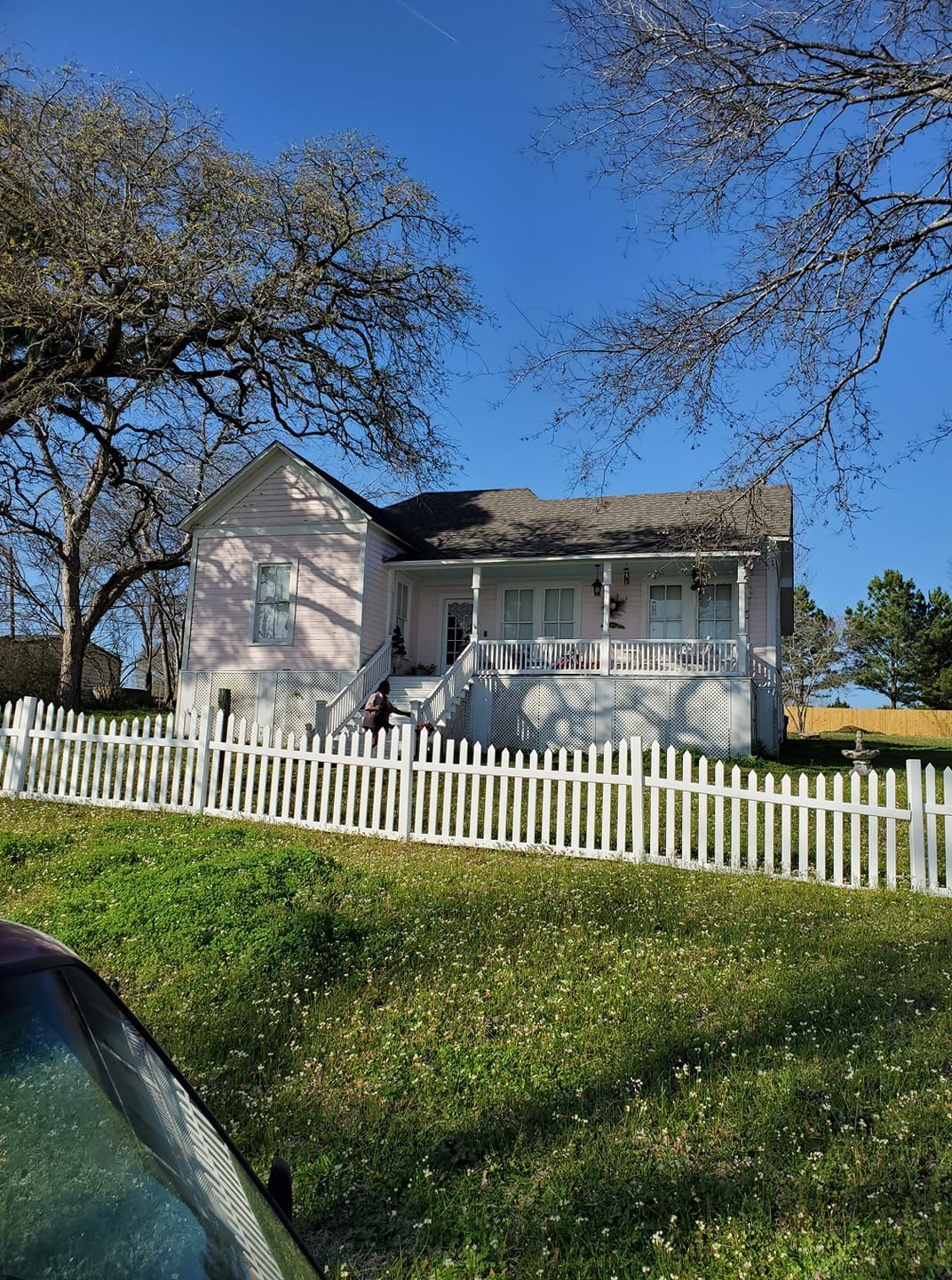 Small white house with a porch and picket fence on a grassy hill under a blue sky.