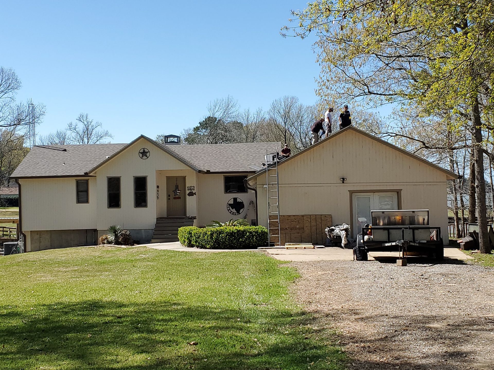 Single-story house with beige garage, gravel driveway, lawn, and truck under a clear blue sky