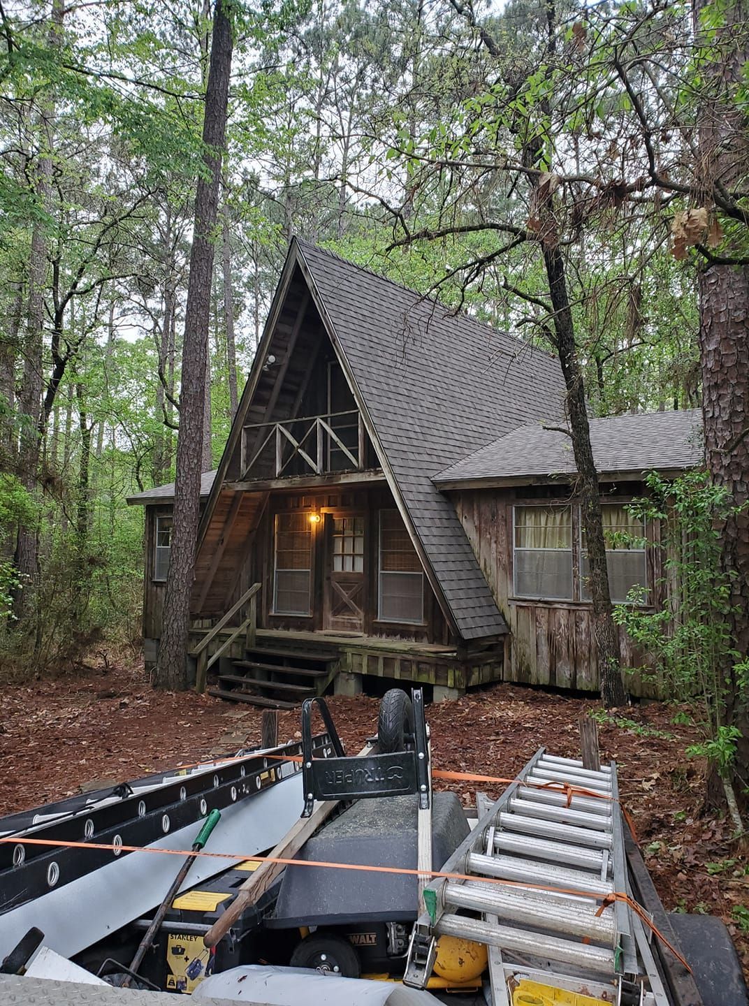 Rustic A-frame cabin in a wooded forest, with a lit porch and construction equipment in front