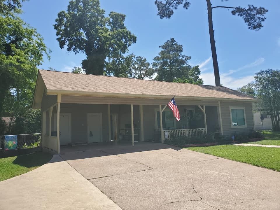 Single-story house with a front porch, American flag, and a wide driveway under a blue sky