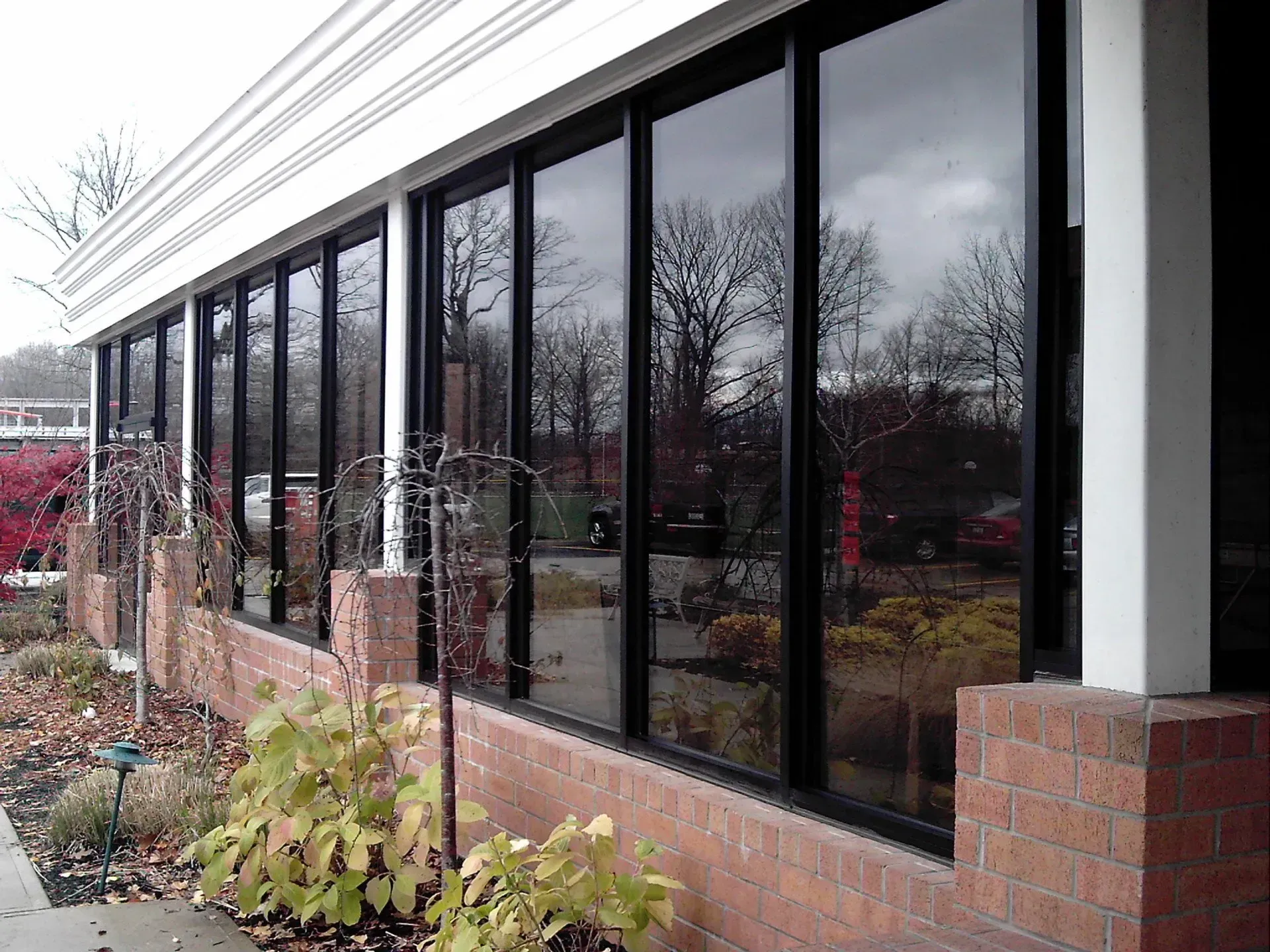 Building with large, dark-tinted windows reflecting the sky and surrounding trees, set against a brick wall.