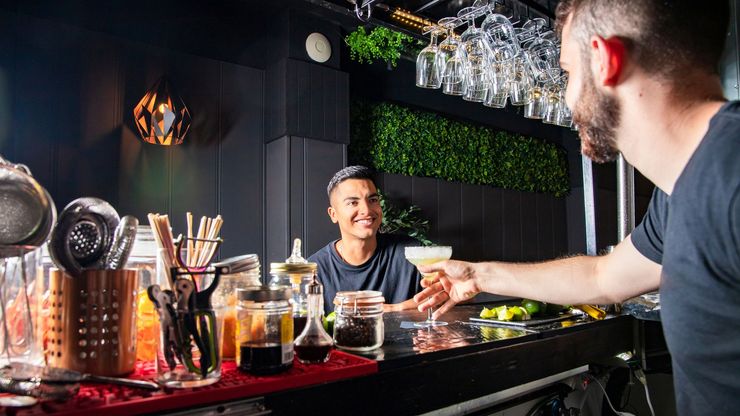 Bartender handing a cocktail to another person at a bar.