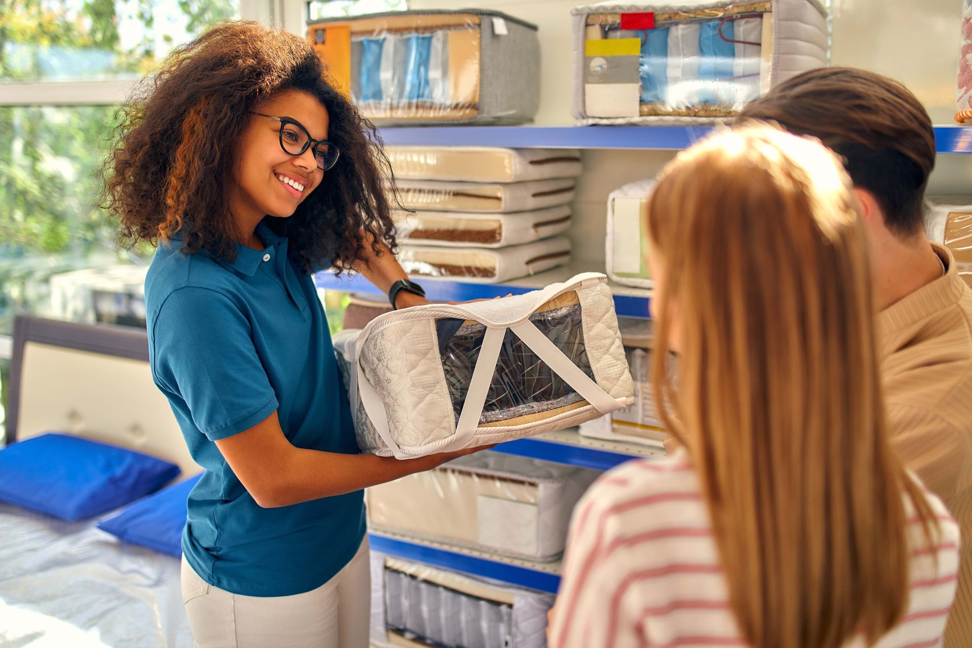 Sales associate shows a wrapped item to a couple in a store; smiling, shelves in the background.