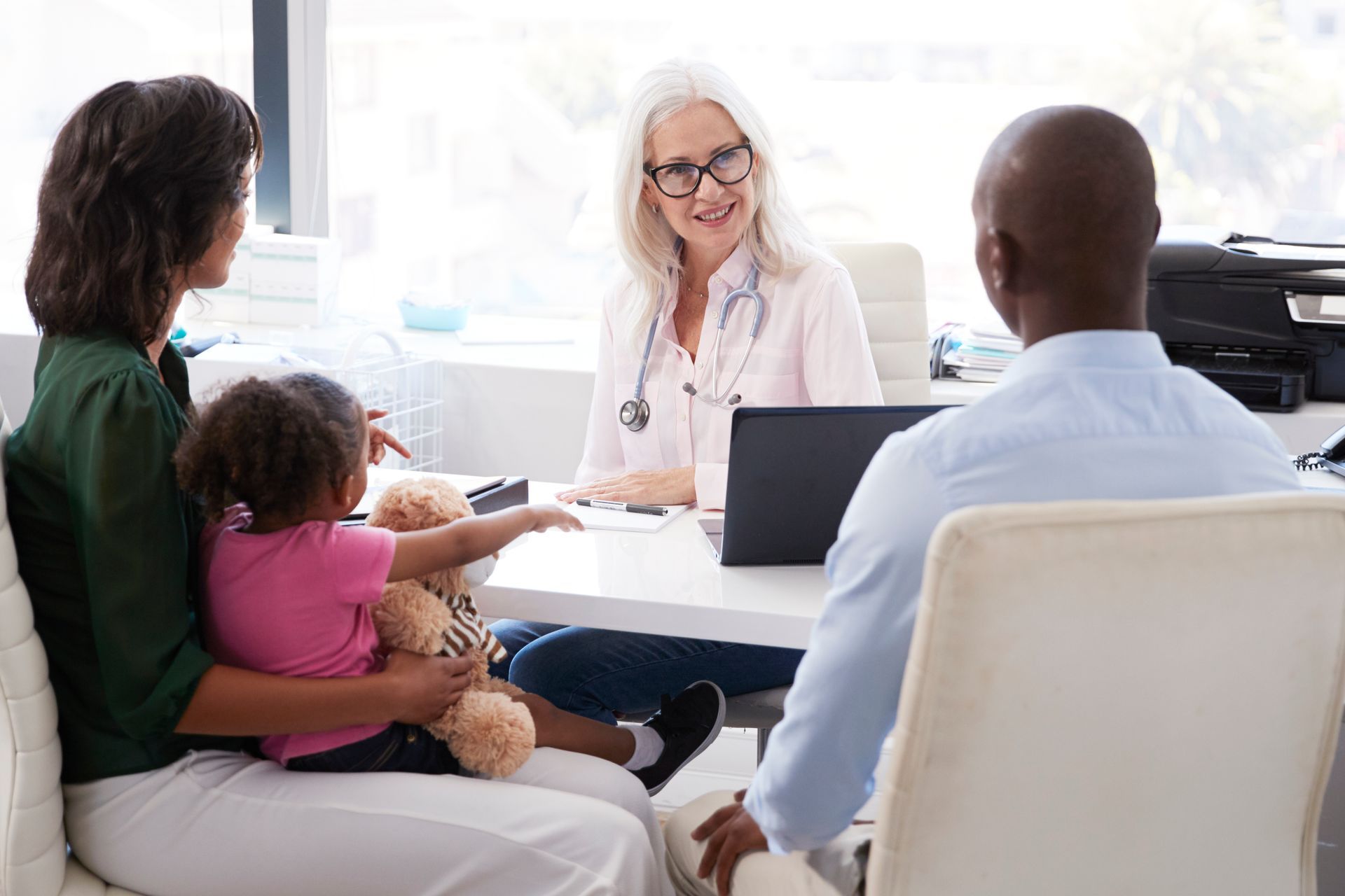 Family with a child at a doctor's appointment; doctor behind a desk with a laptop.