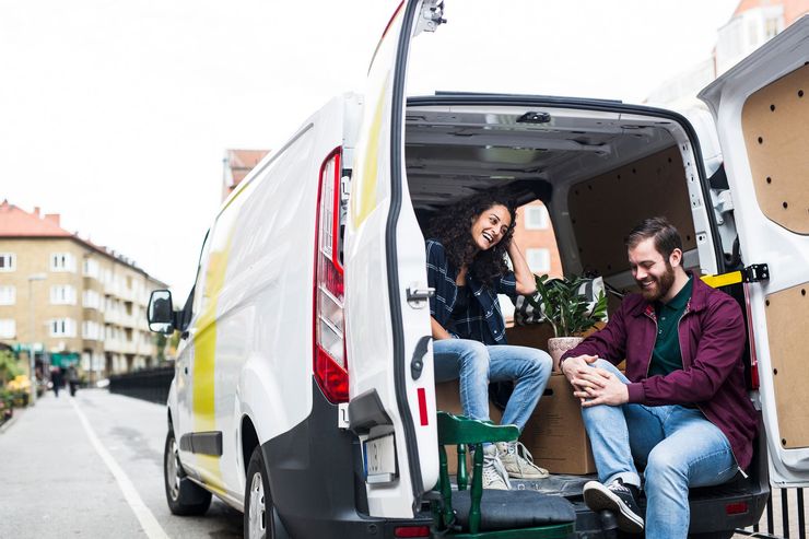 Couple sitting in open back of moving van, smiling, preparing to move belongings.