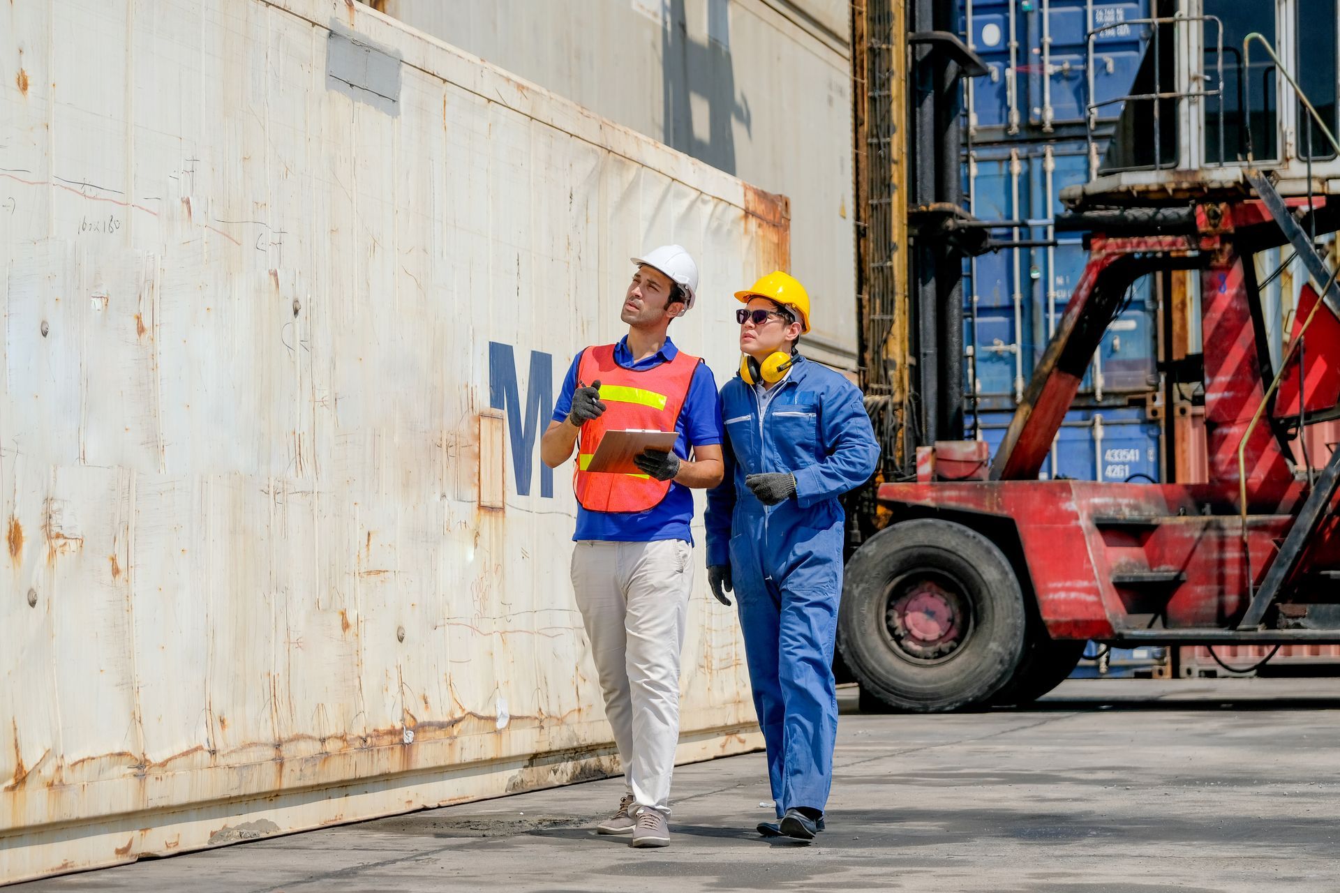 Two workers in safety gear inspecting a shipping container at a port.