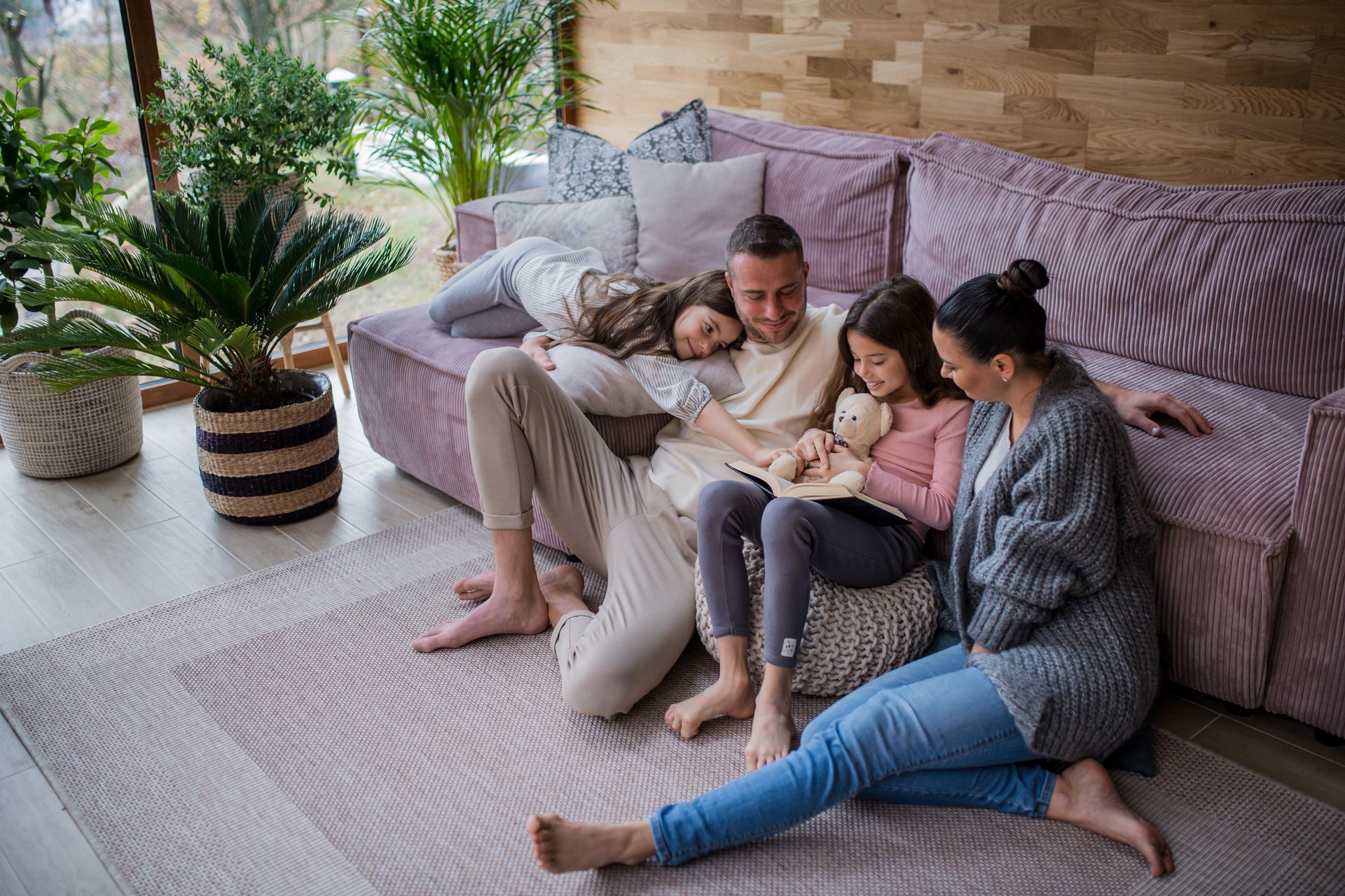 Family relaxing on a couch and floor in a living room with plants.