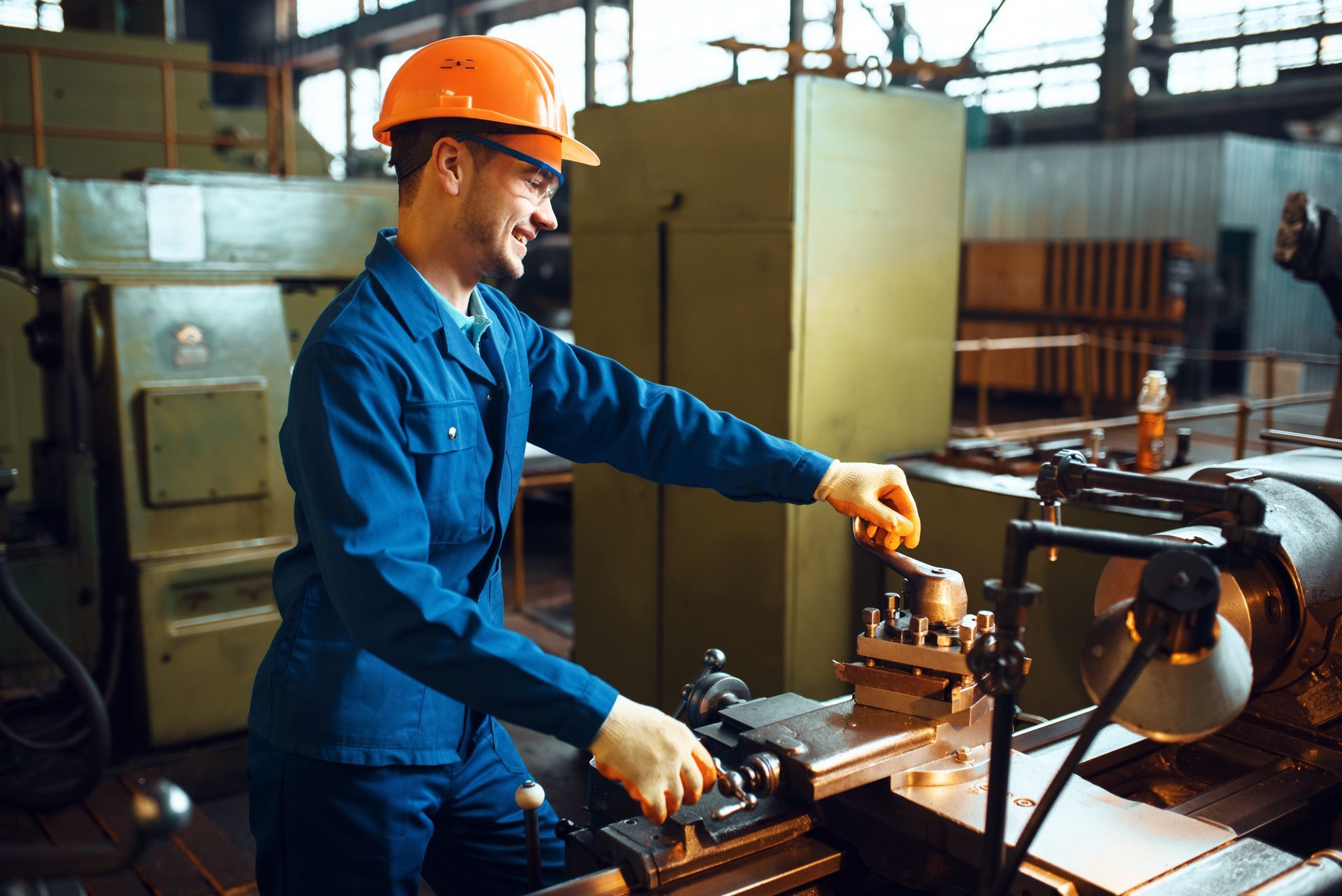 Worker in orange hard hat and blue work suit operates machinery in a factory.