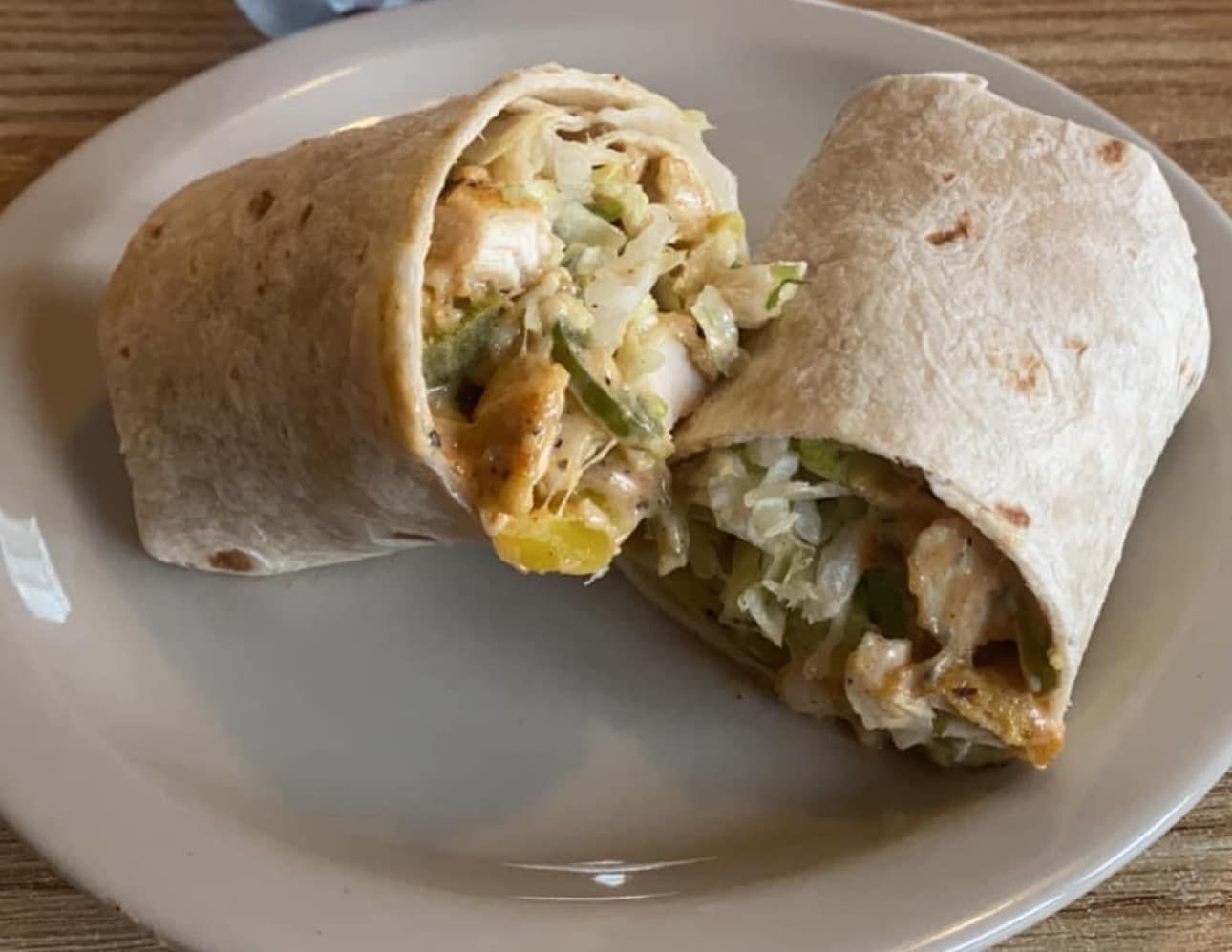 A chicken wrap is cut in half on a white plate
