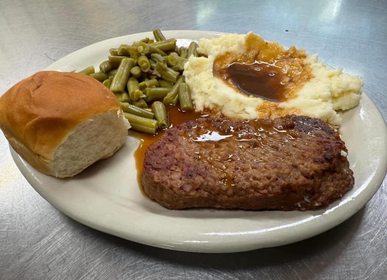 A white plate topped with a meatloaf , mashed potatoes , green beans and a roll.