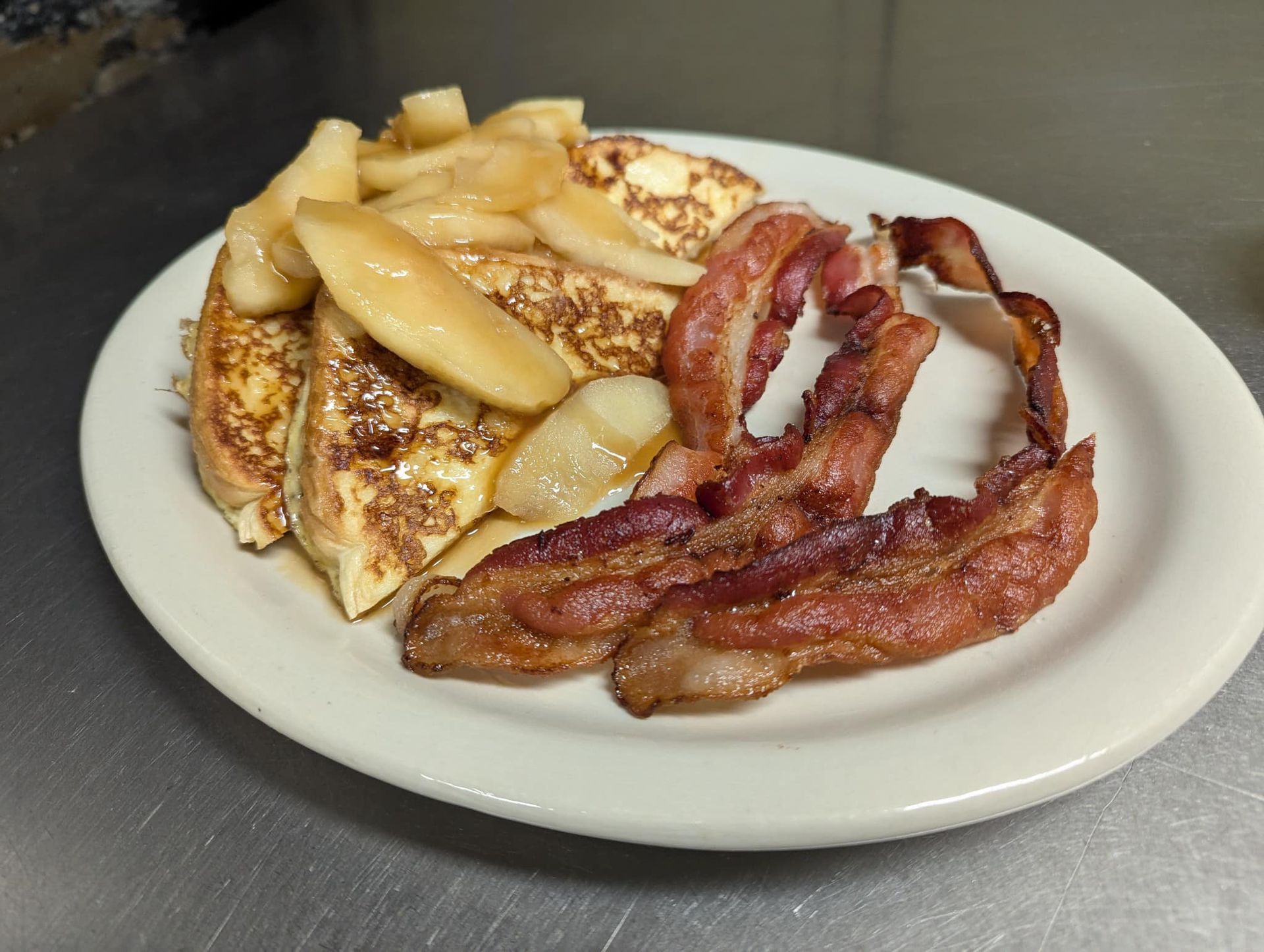 A white plate topped with french toast and bacon on a table.