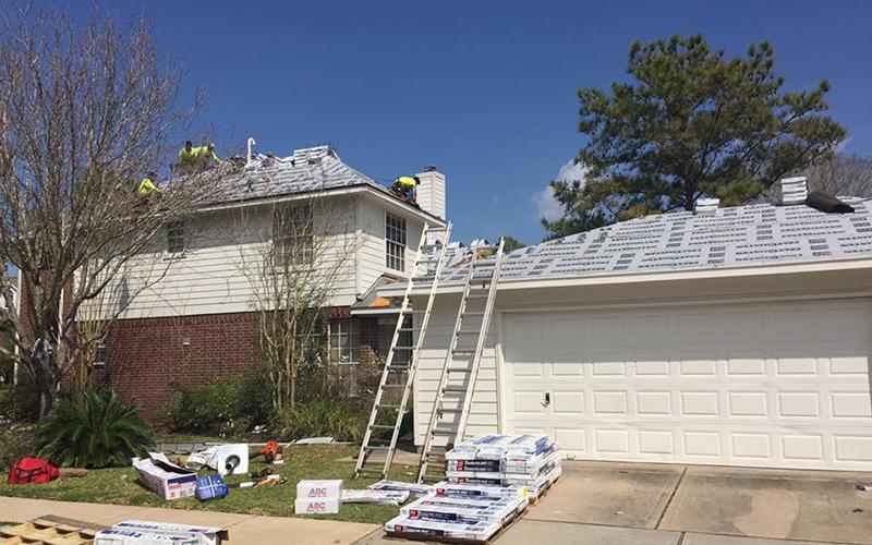 A man is standing on a ladder on the roof of a house.