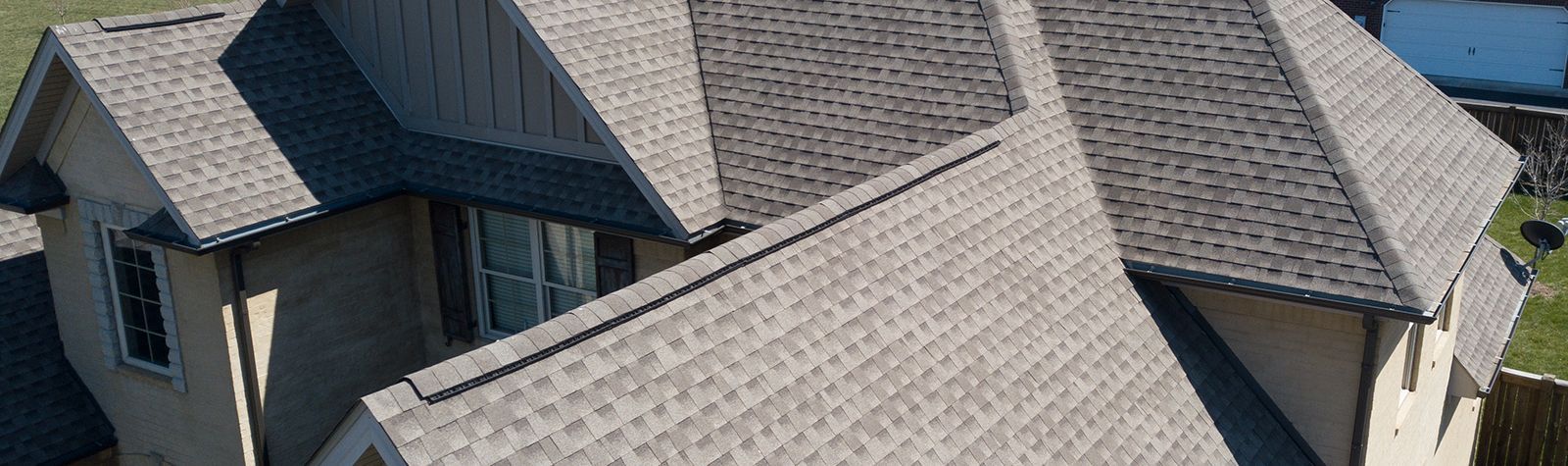 Overhead view of a house with a complex roof structure composed of gray shingles. The walls are beige.