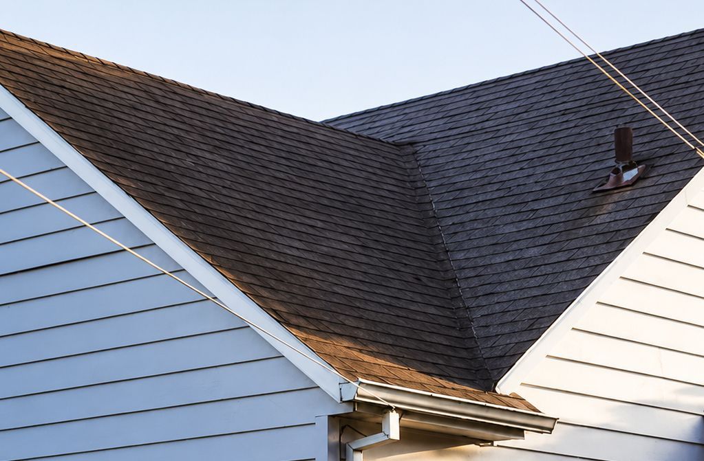 Three adjacent house roofs with dark shingles and white siding under a clear sky