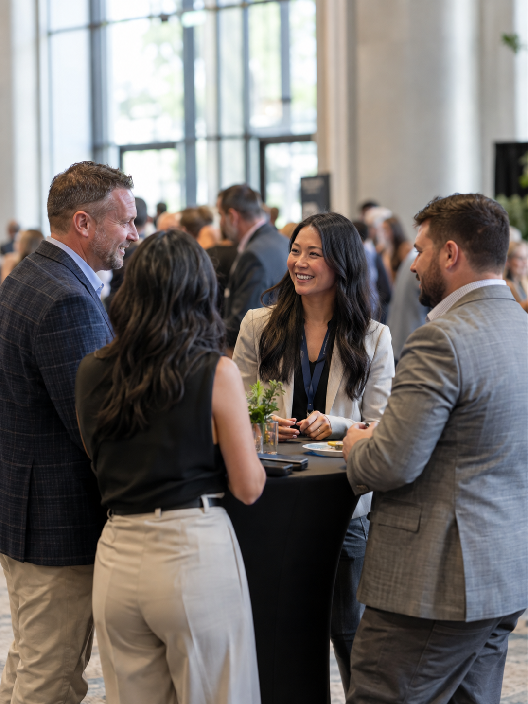 Four colleagues converse at a cocktail table in a bright conference lobby.