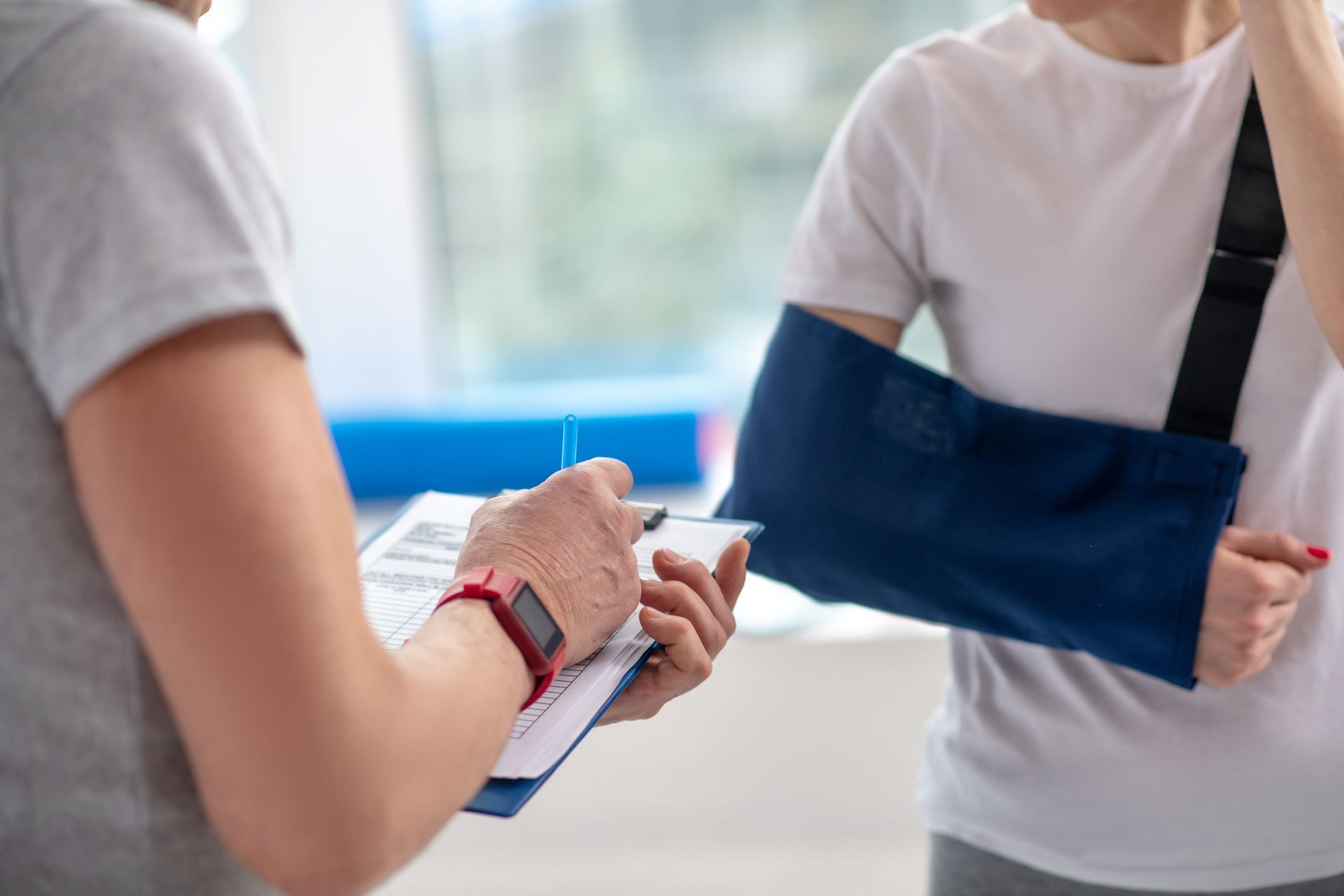 Person with arm in sling being consulted by another person taking notes.
