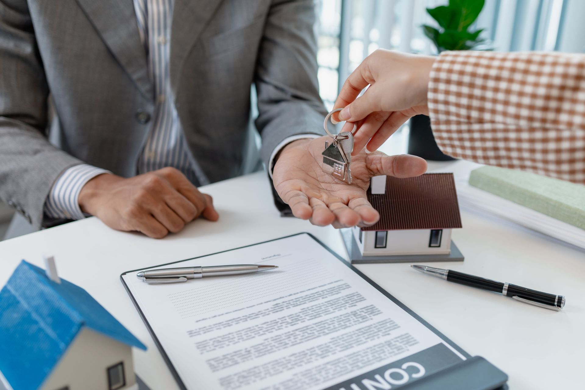 Hands exchange house keys over a signed contract at a desk during a real estate closing