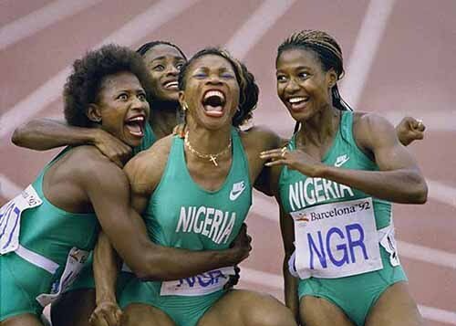 Nigeria relay runners celebrating with arms around each other, smiling in green uniforms.