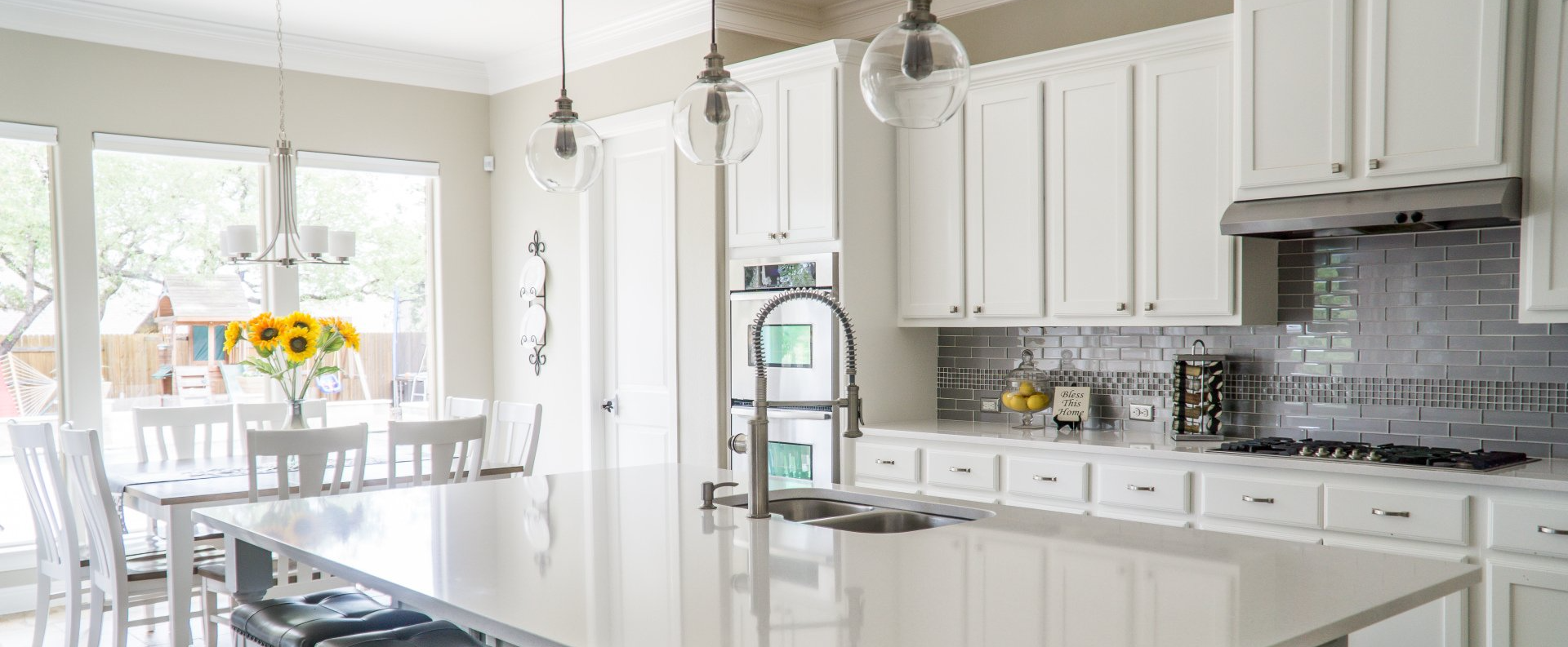 Bright white kitchen with marble island, pendant lights, and a dining table by sunlit windows