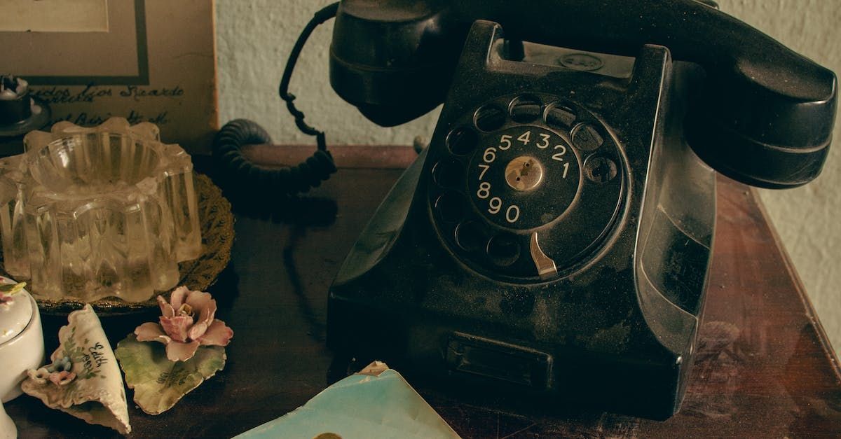 Vintage black rotary phone on a wooden desk beside a glass ashtray and small figurines