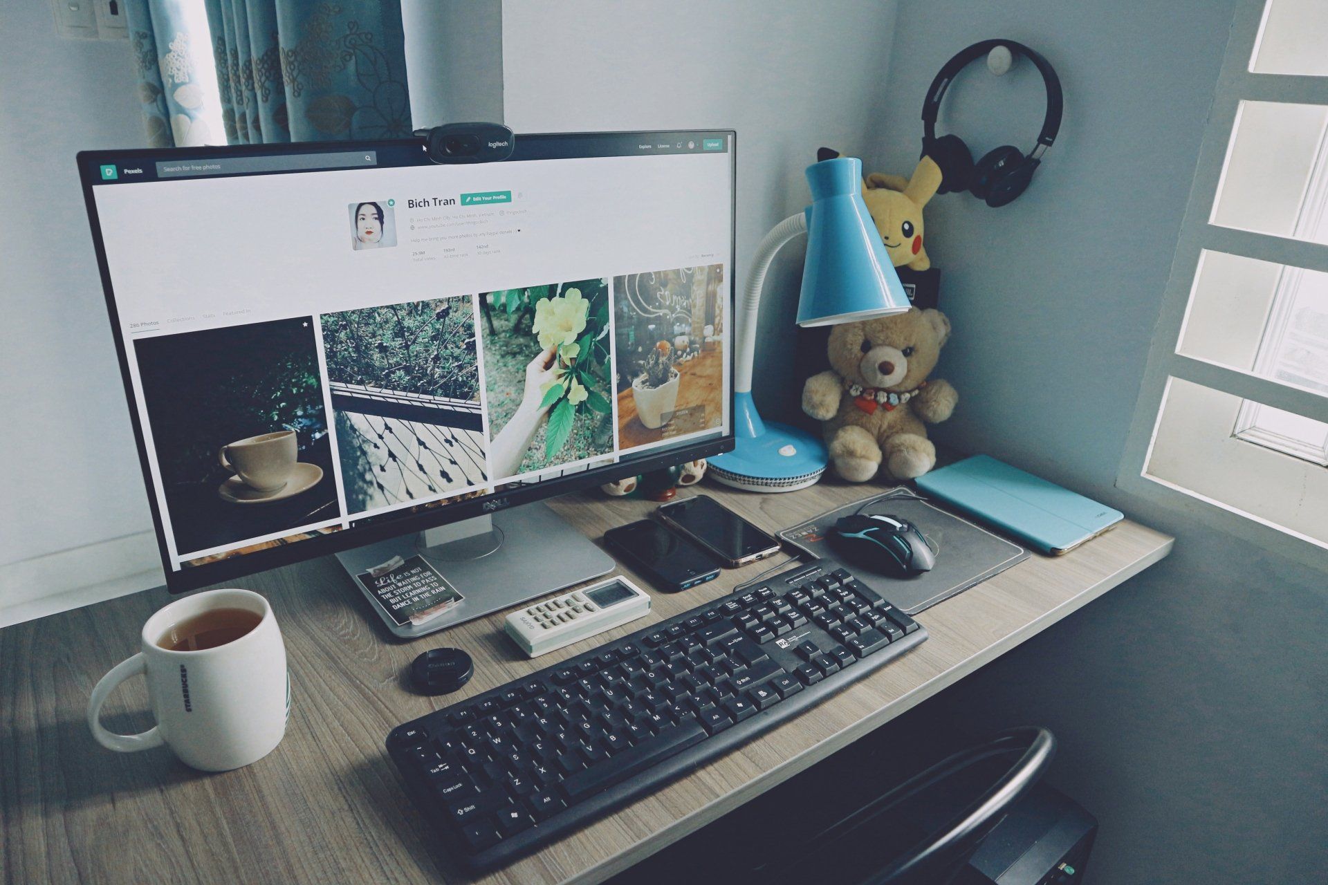 Desktop workspace with large monitor, keyboard, coffee mug, teddy bear, blue lamp, and headphones