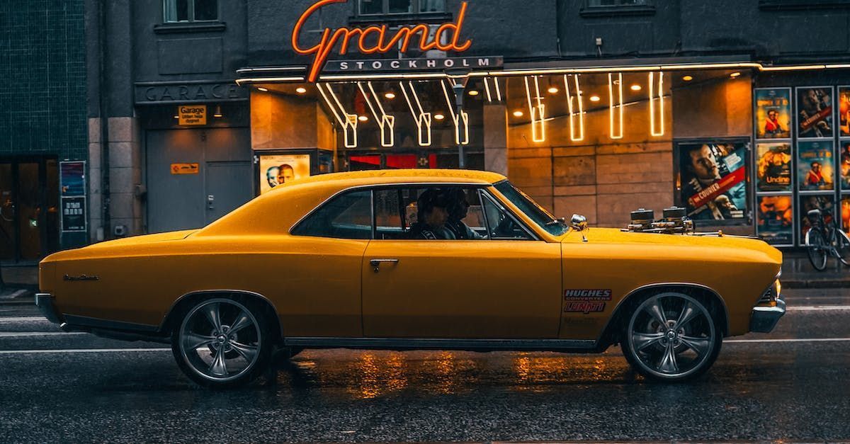 Yellow classic car parked in front of a neon-lit storefront on a rainy street