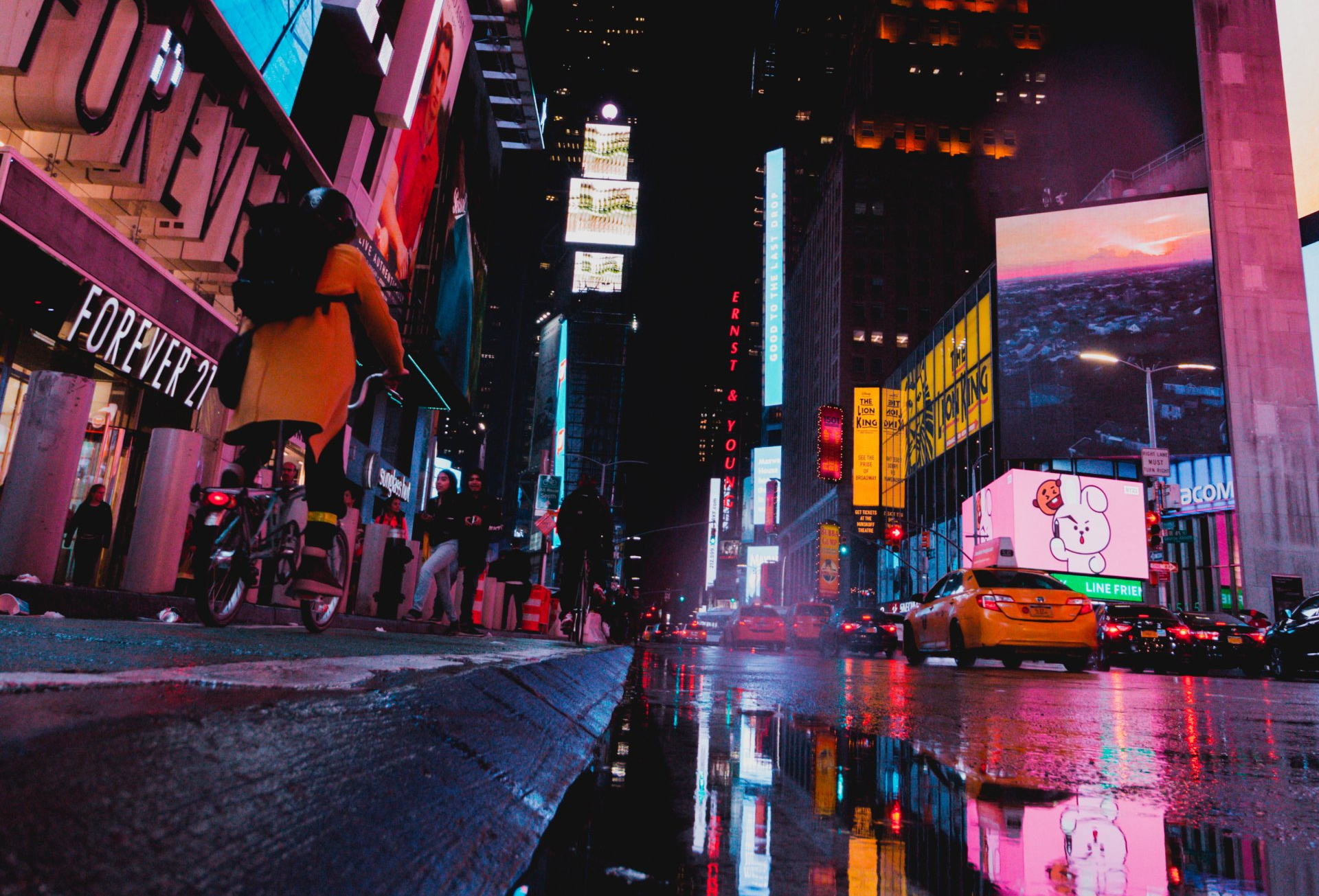Rainy neon-lit city street at night with taxis, tall signs, and reflections on wet pavement