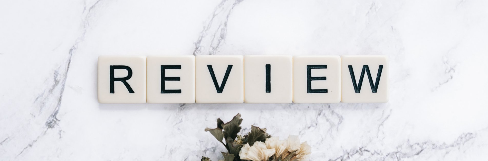 Word “REVIEW” spelled with letter tiles on a white marble surface.