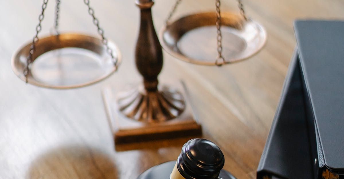 Close-up of a brass balance scale on a desk beside a judge’s gavel and black folder.