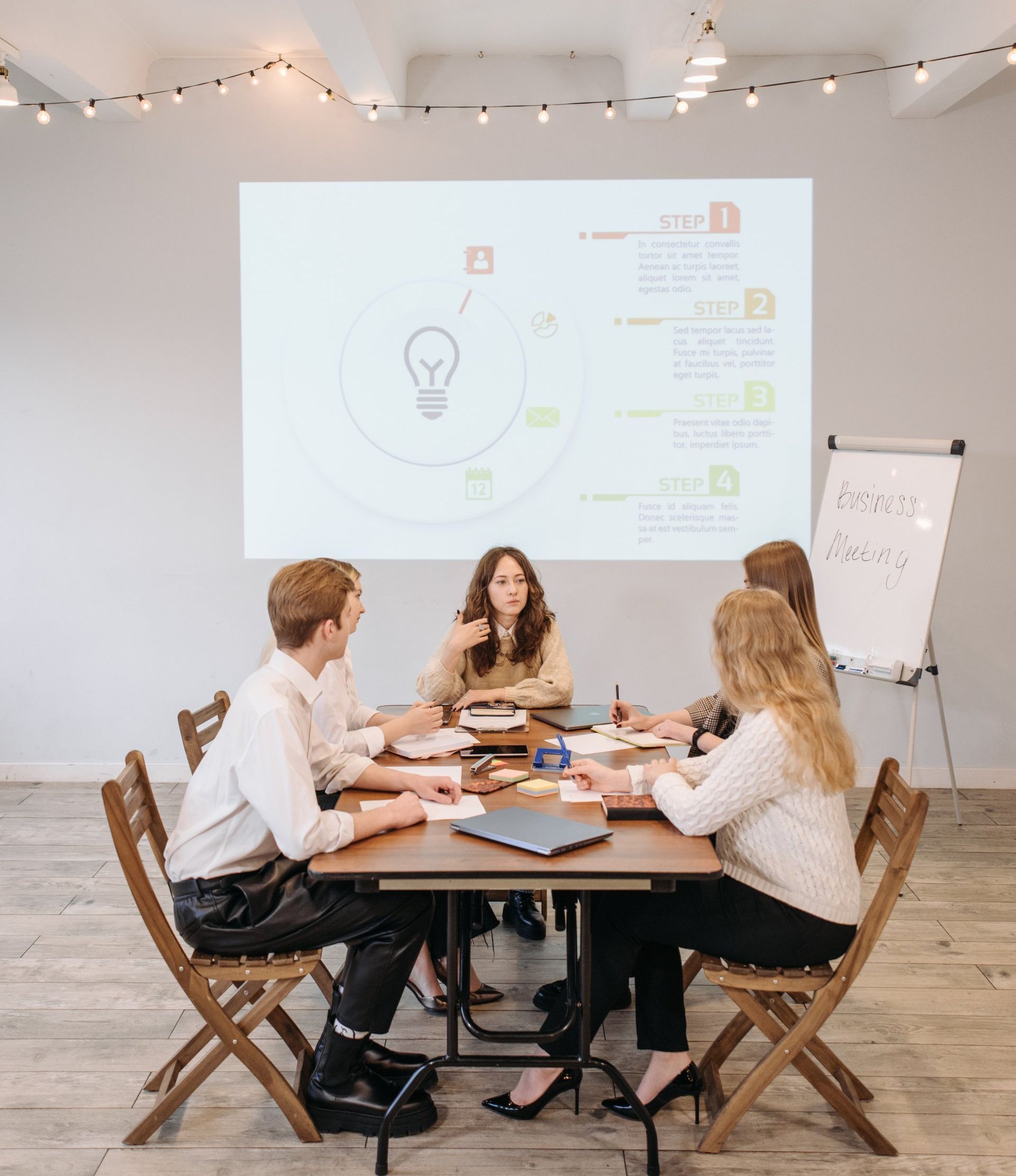 Team meeting around a wooden table in a bright office, with a presentation projected on the wall.