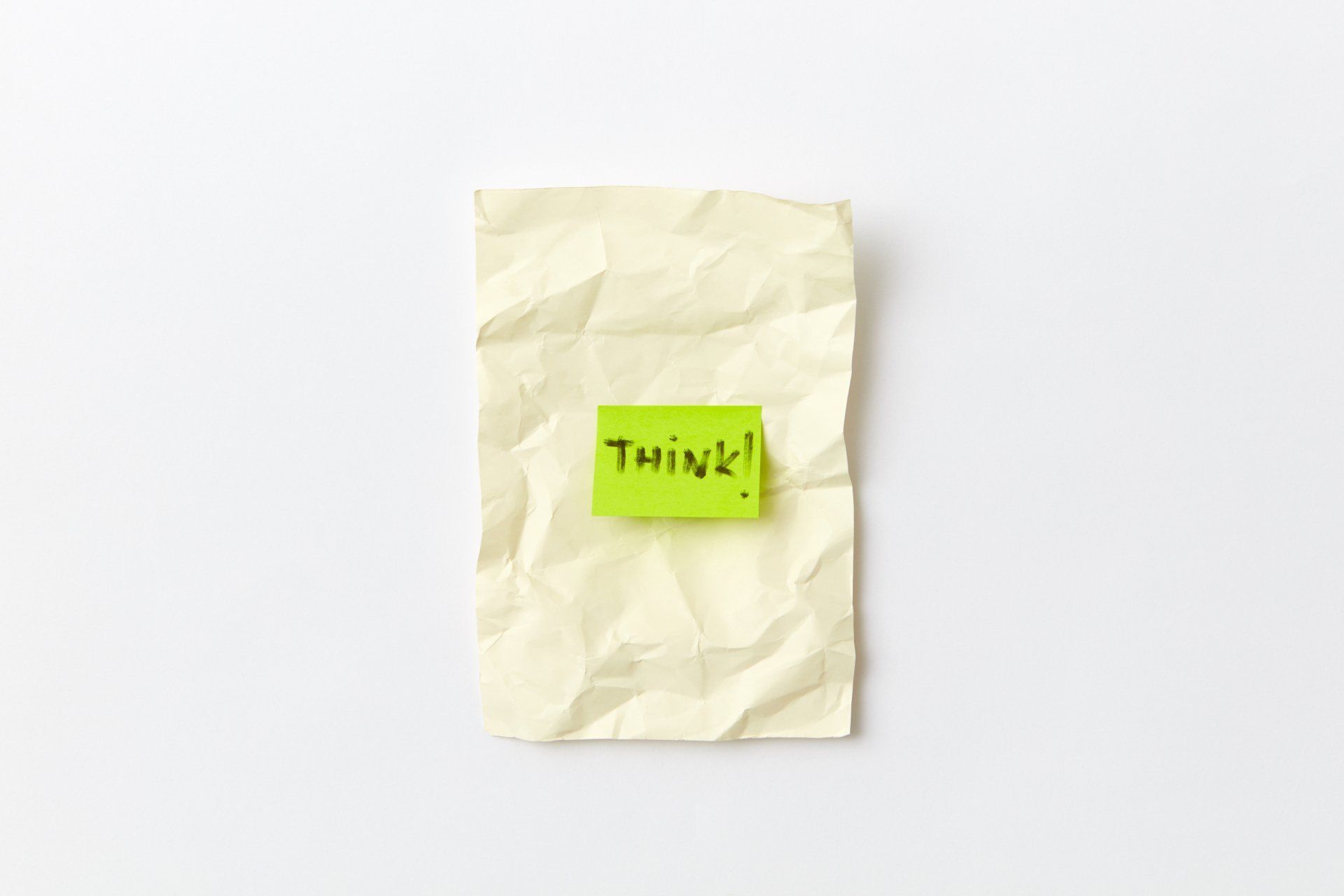 Crumpled white note with a green sticky note reading “Think!” on a plain background