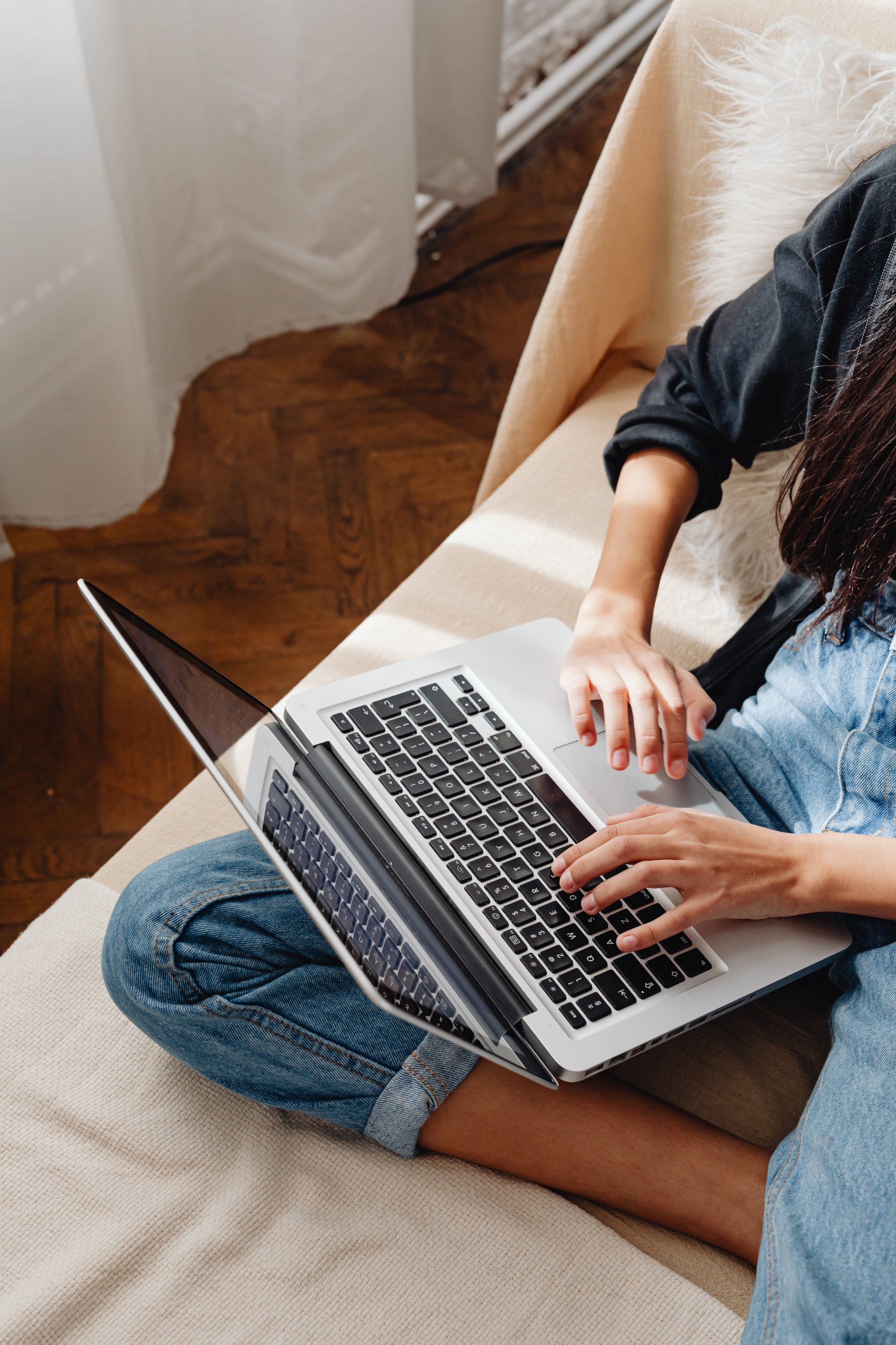 Person using a laptop while seated on a couch near a window