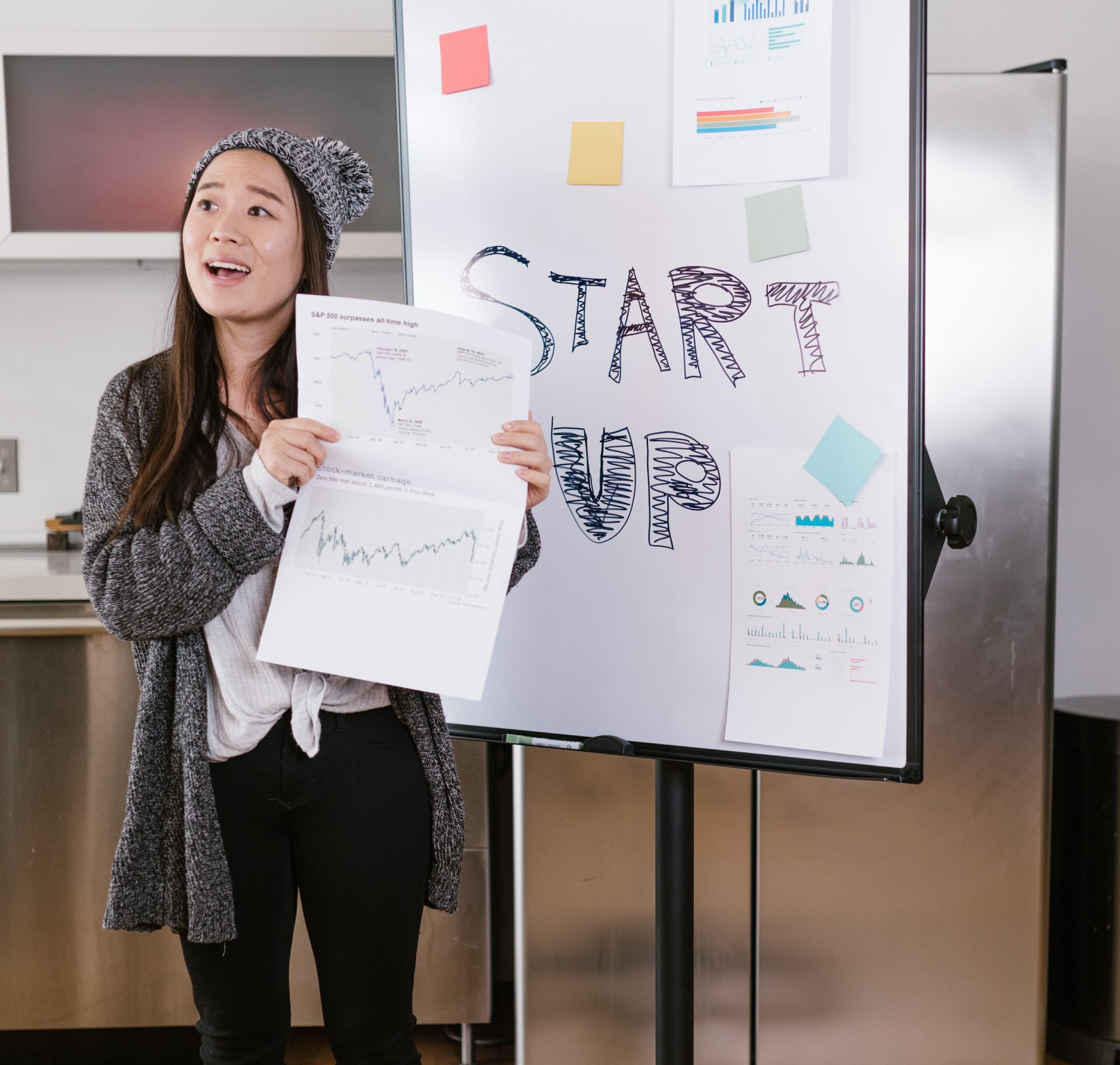Woman presenting charts beside a whiteboard labeled “START UP” in an office setting