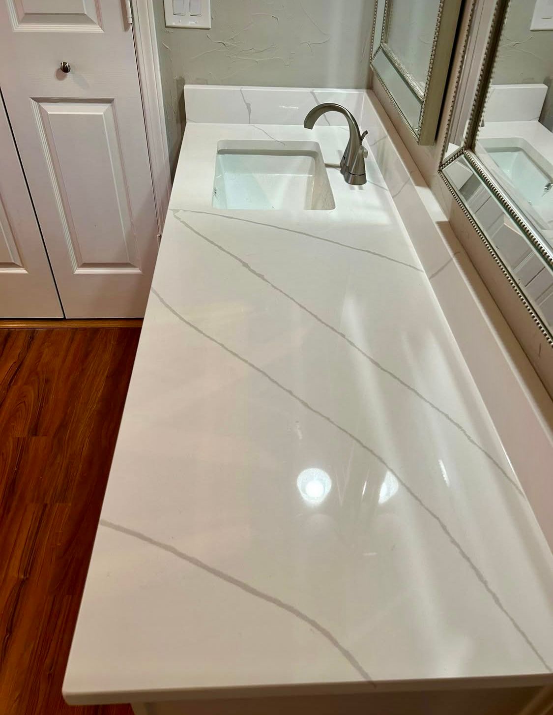 A bathroom vanity with a white quartz countertop, integrated sink, and faucet. The countertop has diagonal gray veining.