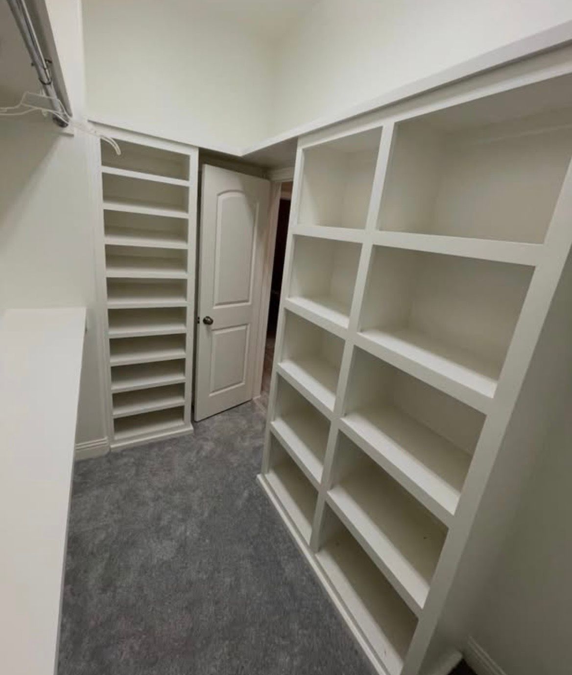 Small walk-in closet with white shelving and gray carpet, viewed toward a closed door.